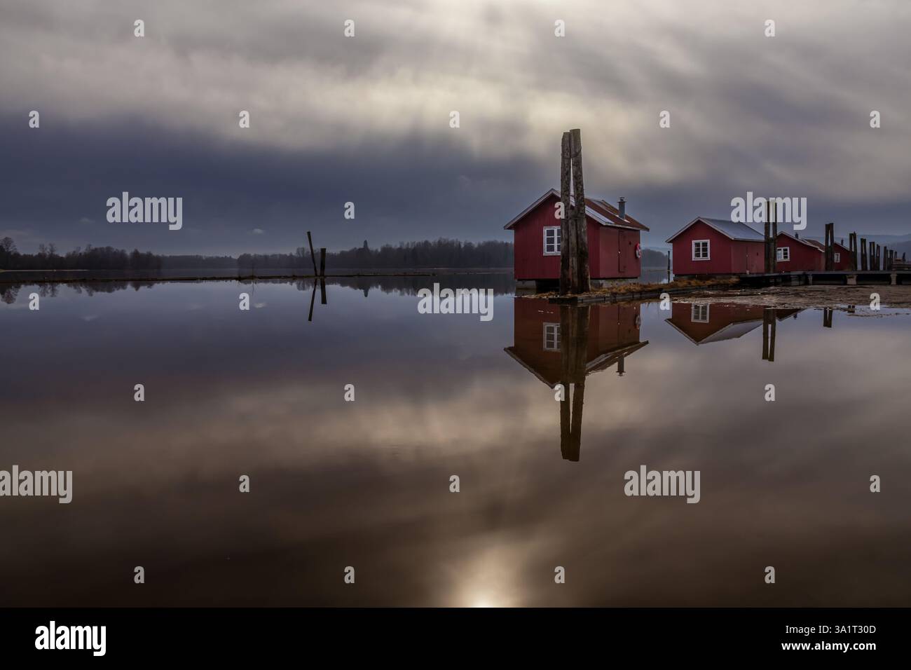 Le vecchie passerelle in legno e le boatouses rosse si riflettono nell'acqua poco profonda, raccontando storie di tempo che passa Foto Stock