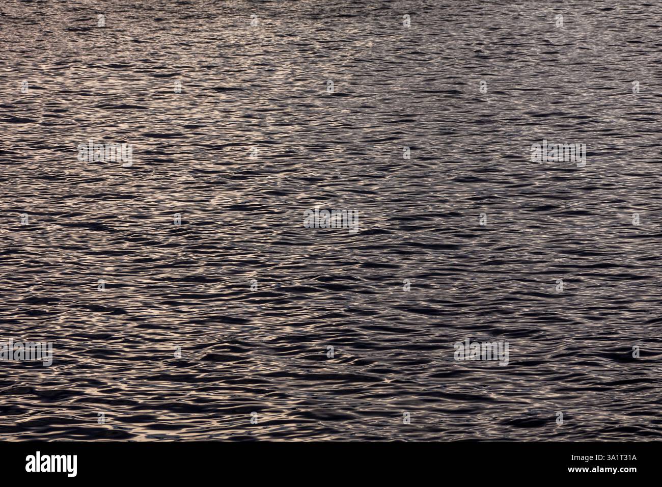 Primo piano dell'acqua del lago o del fiume con morbide ondulazioni che formano colline morbide e ondulate sulla superficie, riflettendo il movimento e la fluidità Foto Stock