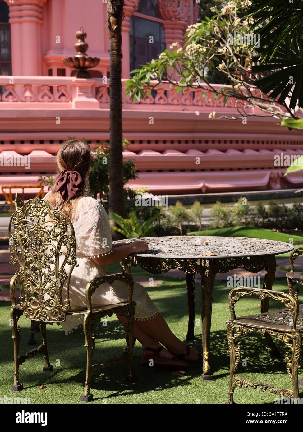 Donna che si rilassa ad un tavolo da giardino vicino a un edificio rosa Foto Stock