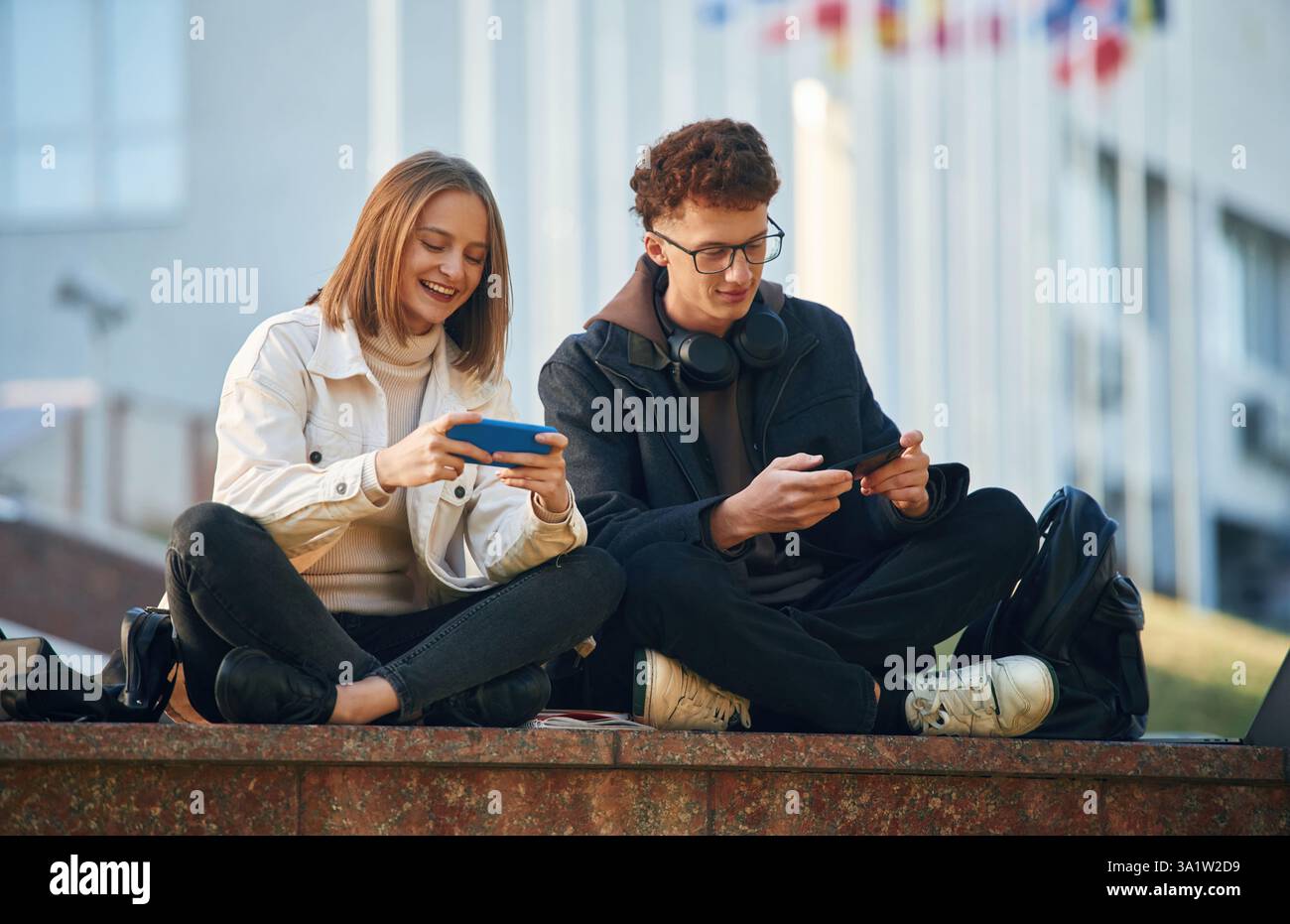 Sorridere, divertirsi. Due giovani studenti sono seduti all'aperto contro l'università. Foto Stock