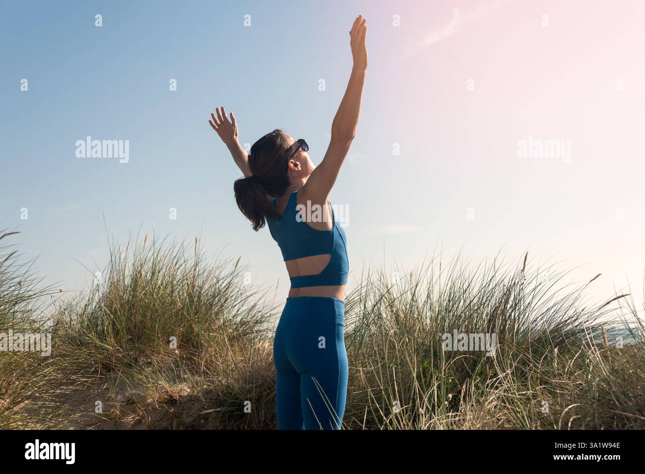donna sportiva in piedi su dune di sabbia con le braccia sollevate al sole Foto Stock