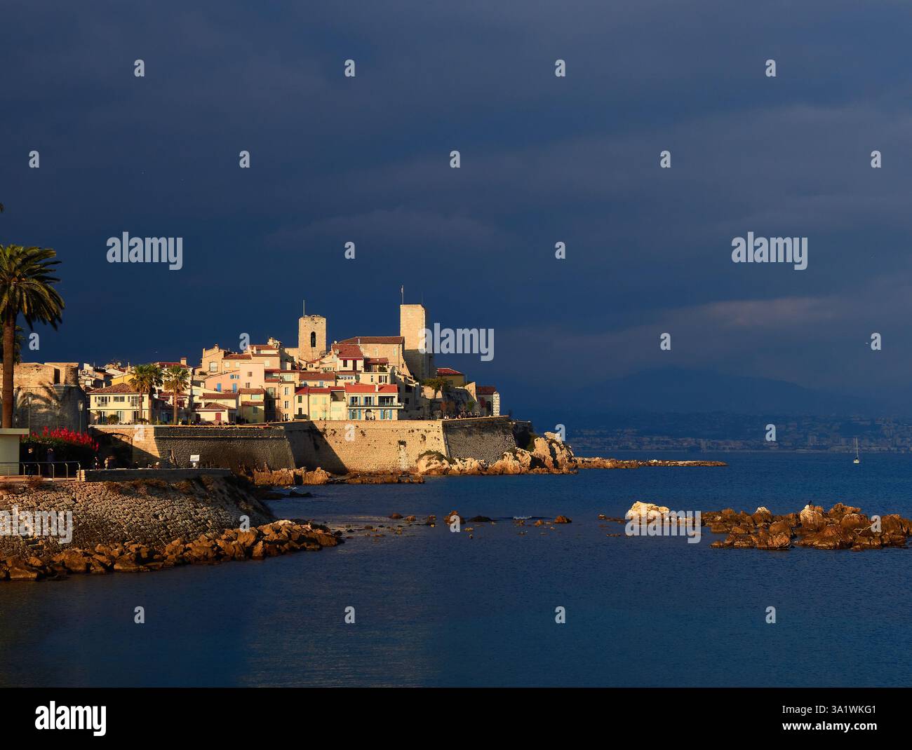 Paesino costiero di Antibes illuminato dal sole con architettura medievale e vista sull'oceano sotto un cielo nero. Foto Stock
