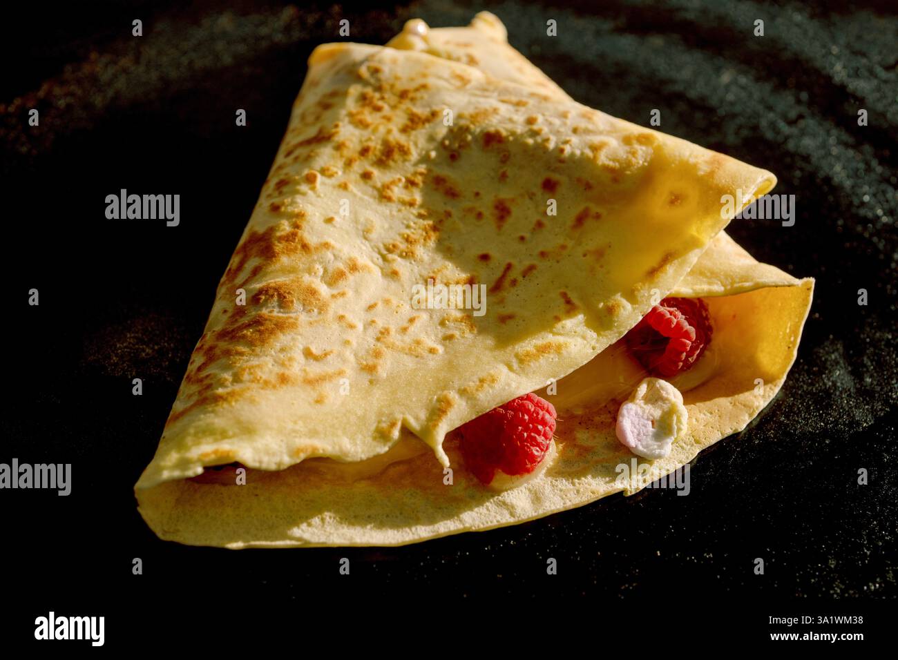 Una deliziosa crepe francese, dorata e sottile, elegantemente avvolta intorno a un miscuglio di frutti di bosco freschi e noci croccanti, gustosi pancake Foto Stock