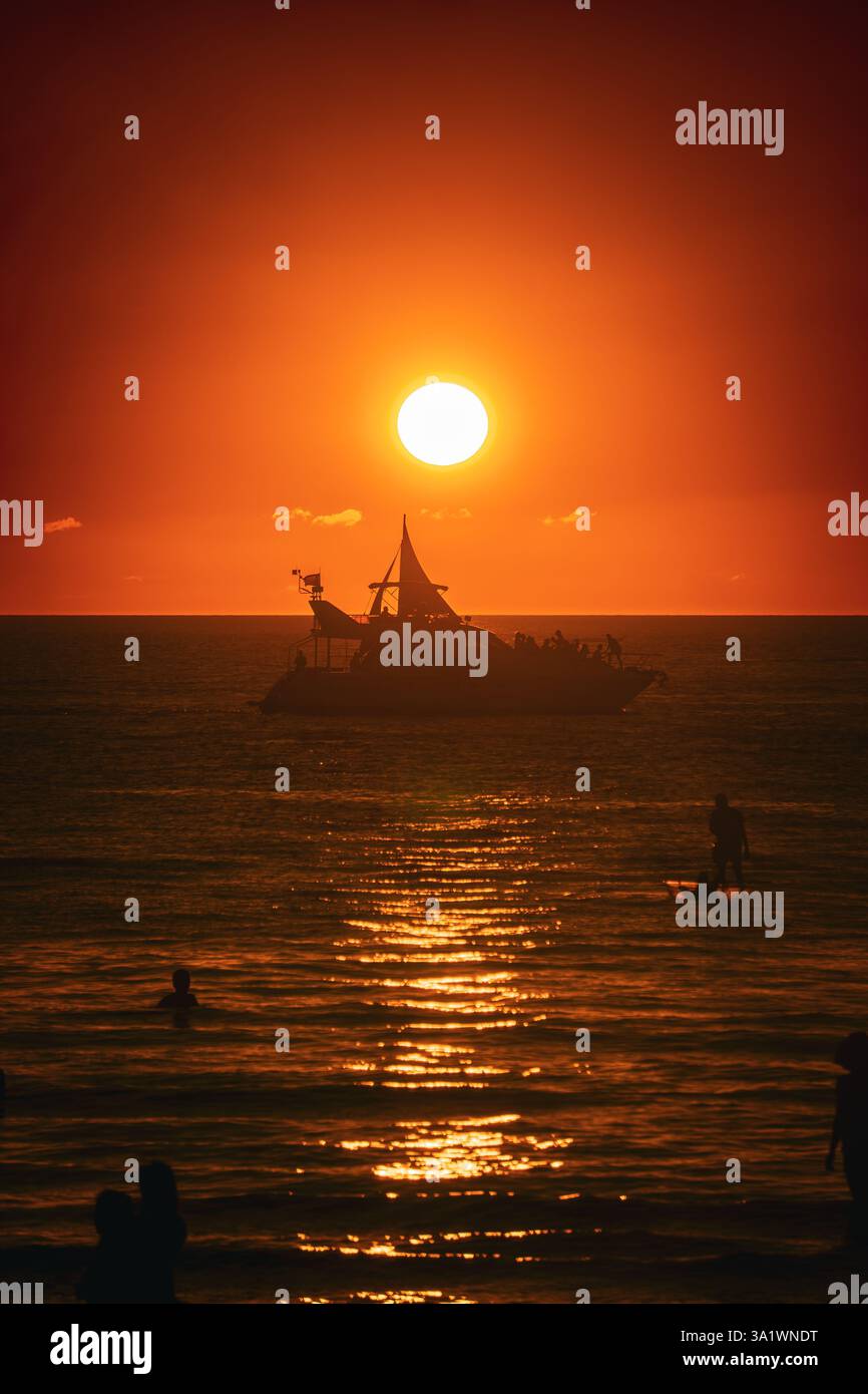 Una barca sagomata contro un vivace tramonto arancione Foto Stock