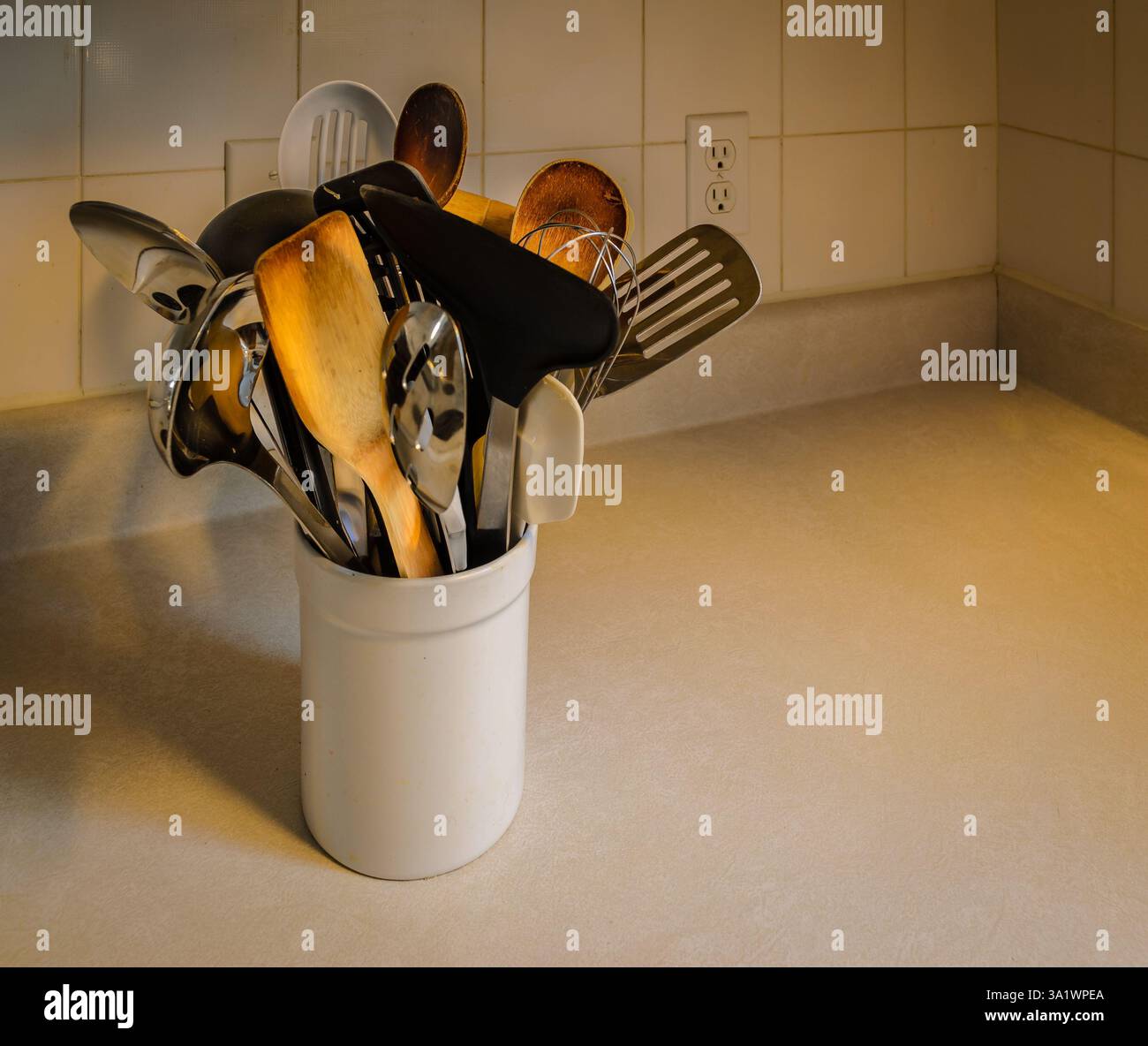 utensili da cucina in vaso bianco in ceramica sul piano di lavoro con piastrelle in ceramica sullo sfondo Foto Stock