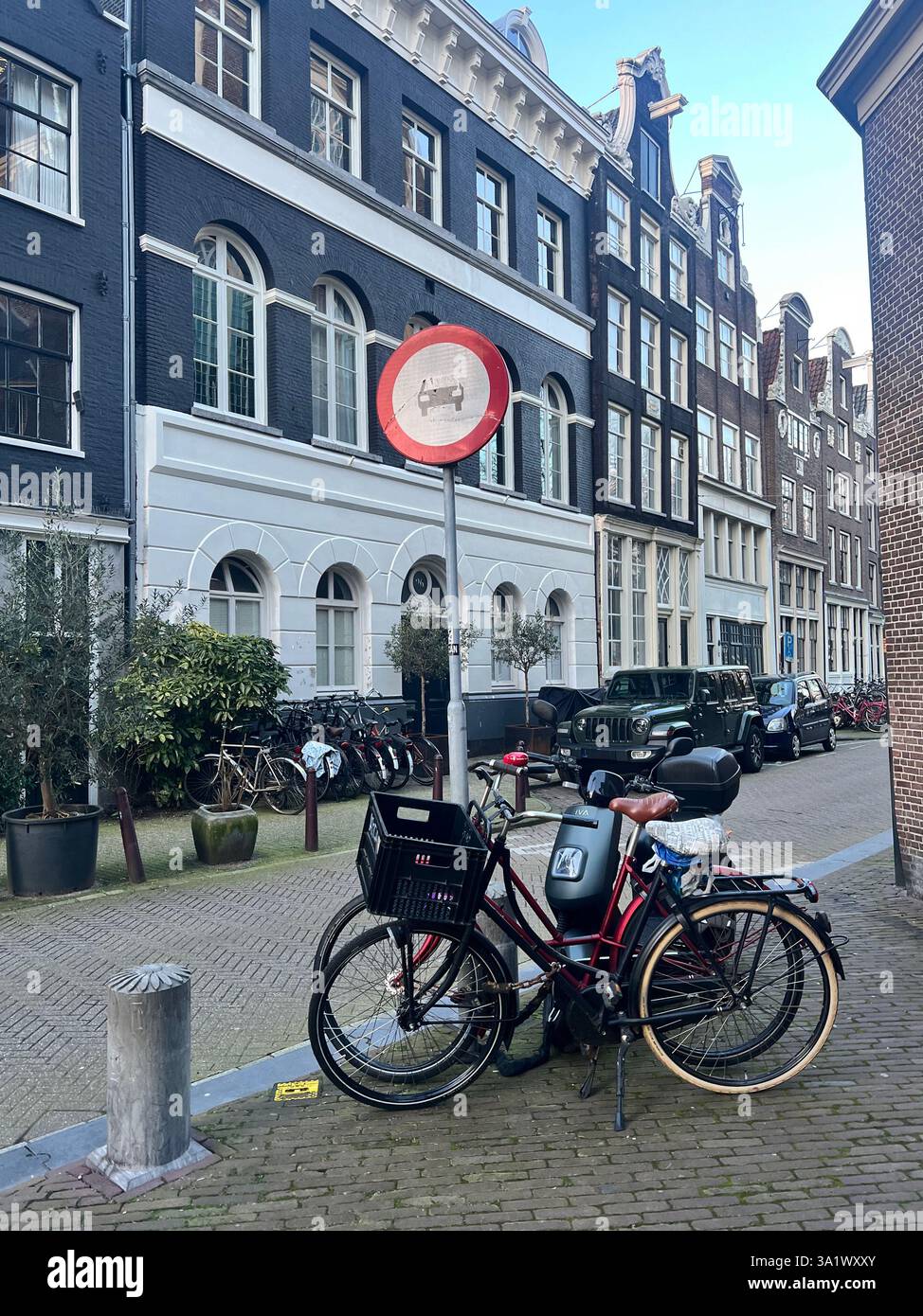 Biciclette classiche olandesi parcheggiate vicino a un cartello senza auto con sullo sfondo l'architettura storica di Amsterdam - Immagine stock catturata con smartphone