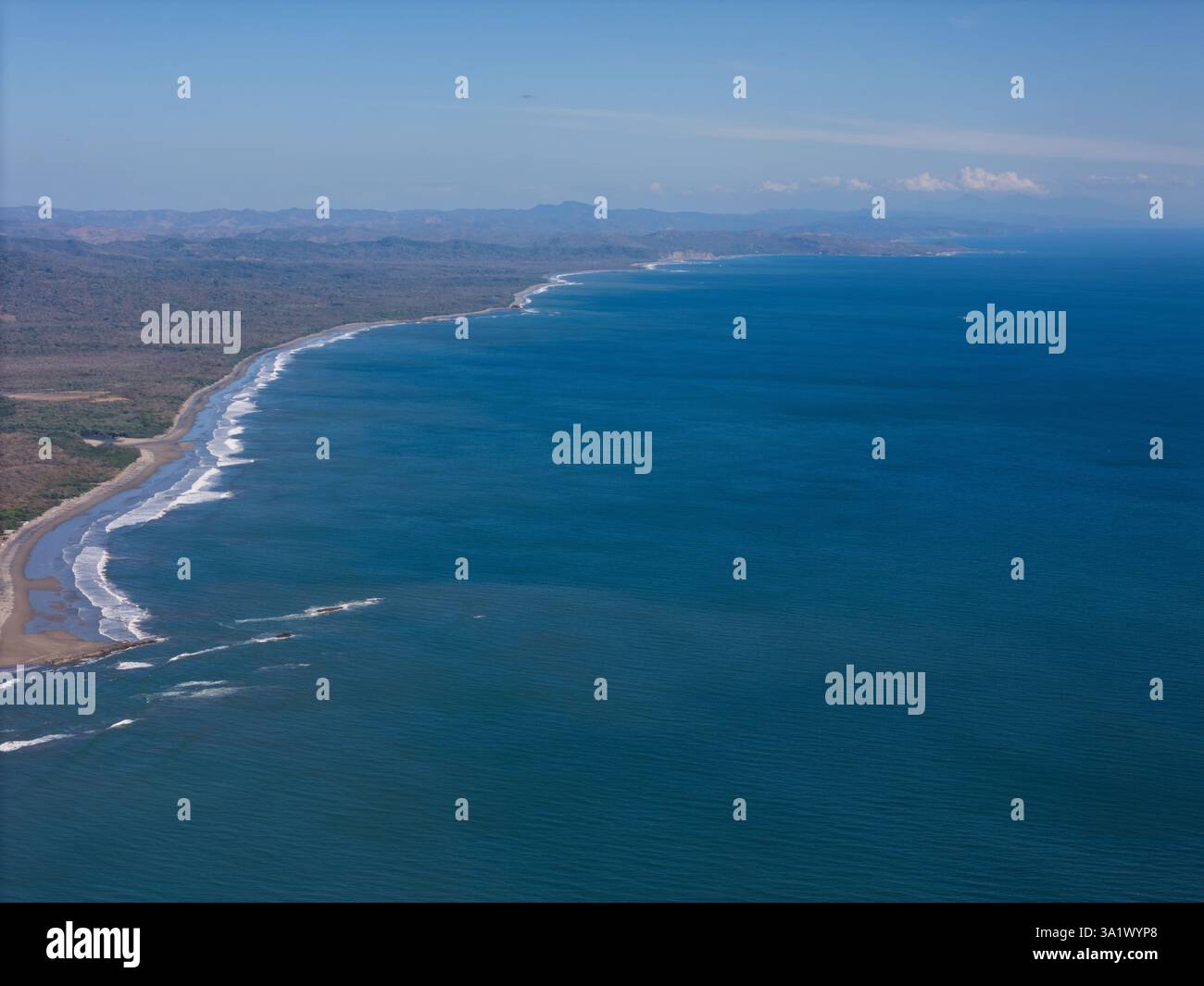 Le onde si infrangono dolcemente sulla spiaggia sabbiosa, incorniciata da scogliere e cieli limpidi lungo la vivace costa. Foto Stock