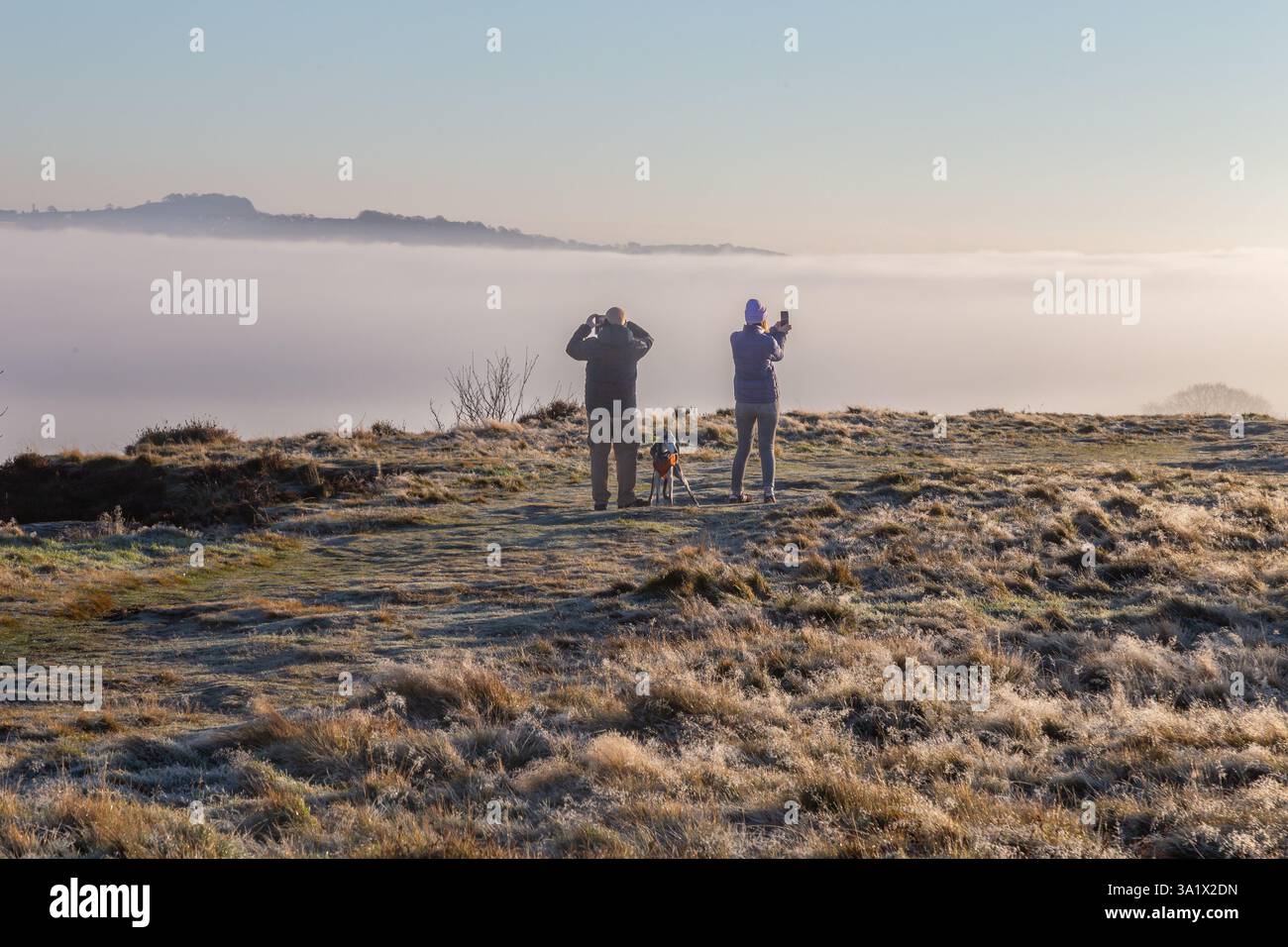 Una coppia (uomo e donna) sta usando i loro telefoni cellulari (smartphone) per fotografare una nuvola invertita di Baildon Moor nello Yorkshire. Foto Stock