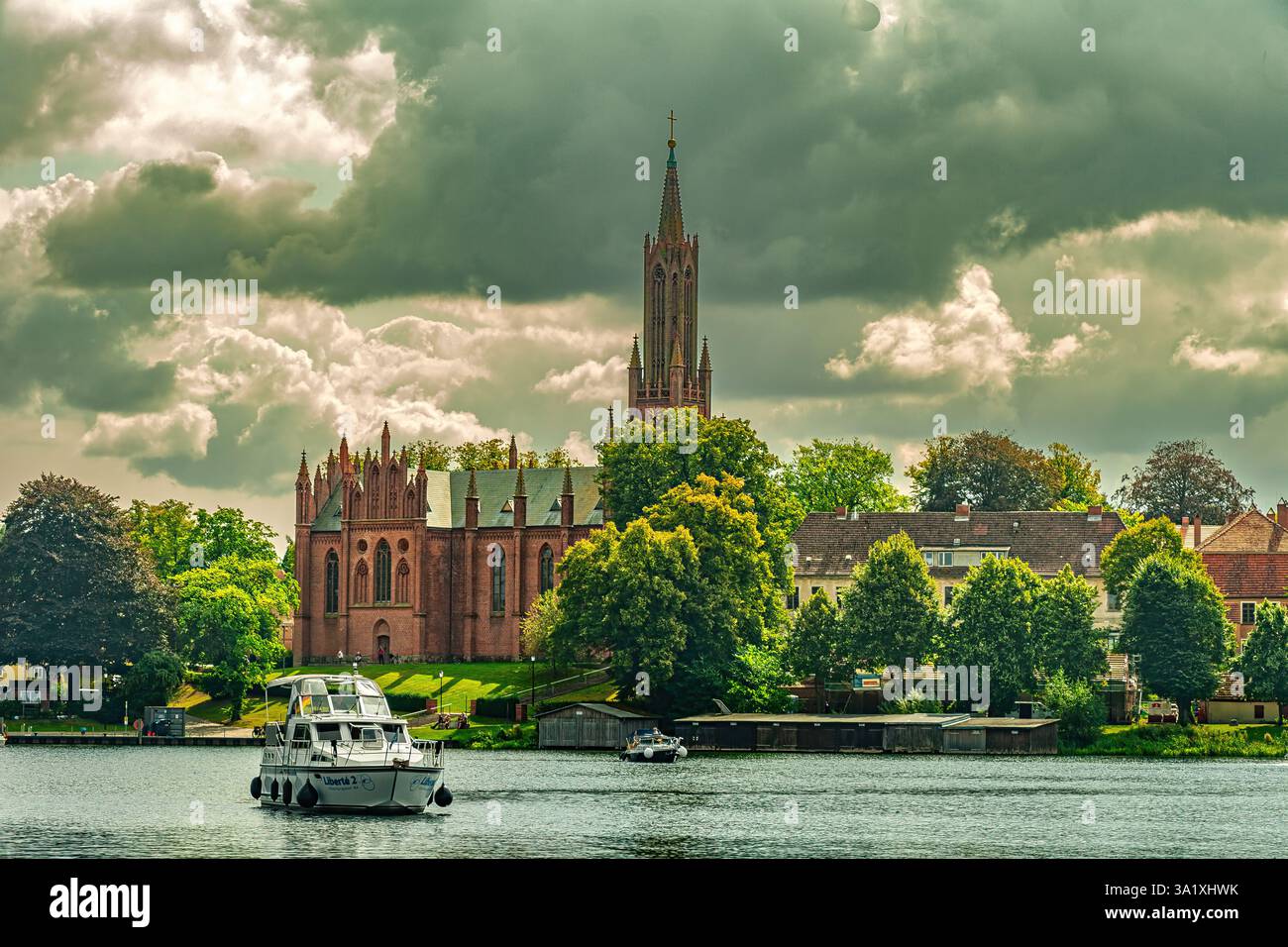 Barca a motore sul tranquillo lago Malchow, la storica chiesa di Klosterkirche incornicia un paesaggio pittoresco nella Germania settentrionale. Malchow Foto Stock