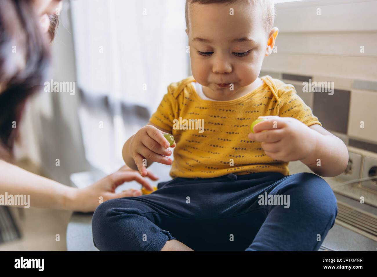 Mamma che dà da mangiare al bambino uva fresca da un sacchetto di carta ecocompatibile, sottolineando la sostenibilità. Foto di alta qualità Foto Stock