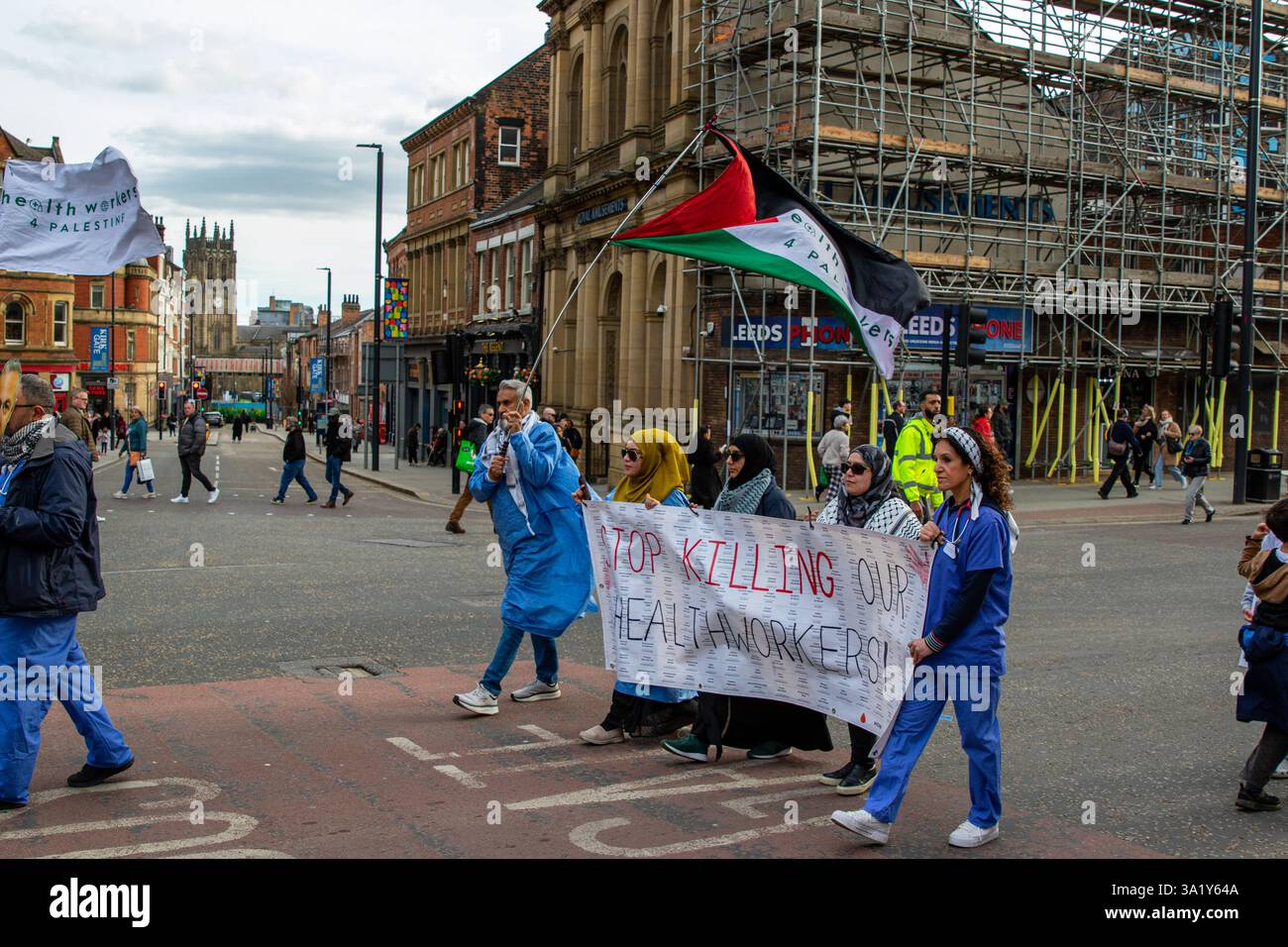 Dimostrazione in una strada della città con persone che tengono in mano cartelli e una bandiera palestinese, con altri pedoni ed edifici della città sullo sfondo. Foto Stock