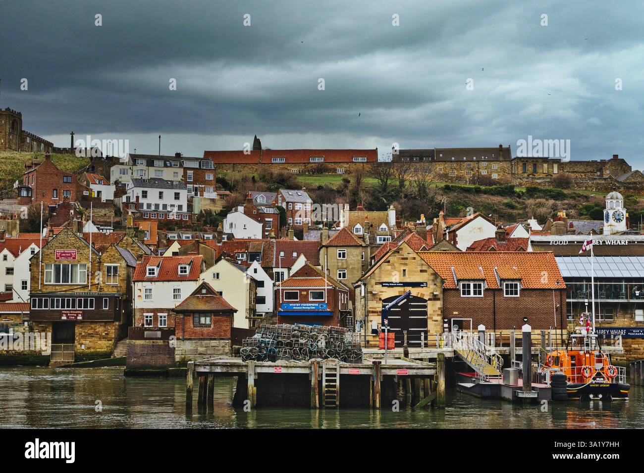 Whitby, paesaggio urbano dell'Inghilterra con edifici, un porto con barche e un cielo scuro e nuvoloso, composto da un leggero angolo verso l'alto. Foto Stock