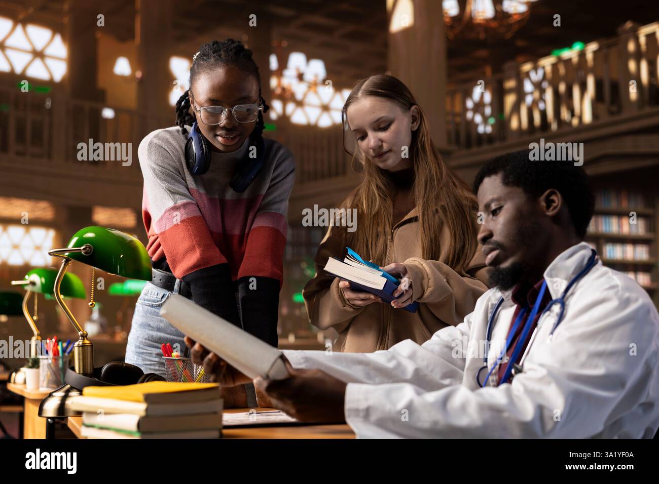 Diversi gruppi di studenti si impegnano in una discussione con il tutor medico, utilizzando libri di testo e note di classe. Utilizzando le risorse della biblioteca universitaria per espandere le loro conoscenze mediche sulla ricerca di medicina. Foto Stock