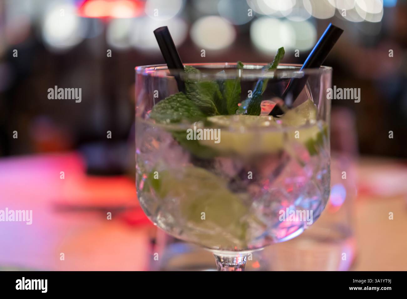 cocktail di mojito rinfrescante in un bicchiere trasparente, guarnito con foglie di menta fresca e fette di lime. La bevanda è servita con due cannucce nere e ghiaccio, set Foto Stock cocktail di mojito rinfrescante in un bicchiere trasparente, guarnito con foglie di menta fresca e fette di lime. La bevanda è servita con due cannucce nere e ghiaccio, set Foto Stock