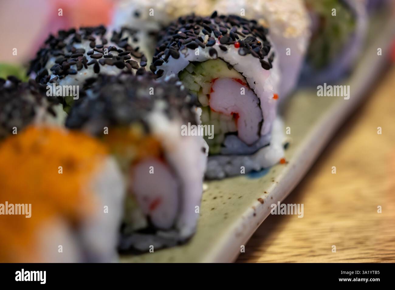 piatto di sushi con vari condimenti e ripieni, disposti su un tavolo di legno. Il sushi è decorato con semi di sesamo nero, semi di sesamo bianco Foto Stock