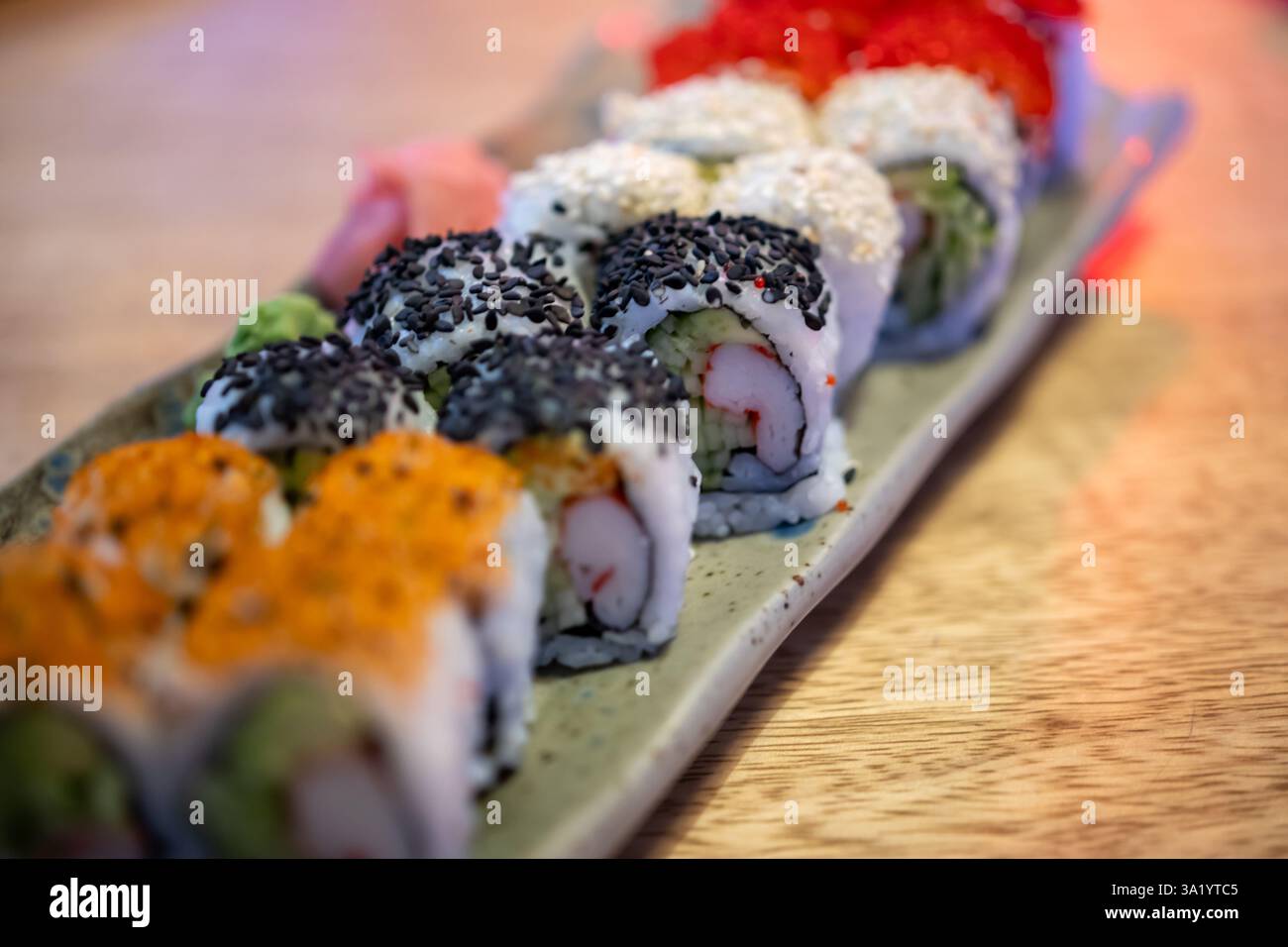 piatto di sushi con vari condimenti e ripieni, disposti su un tavolo di legno. Il sushi è decorato con semi di sesamo nero, semi di sesamo bianco Foto Stock