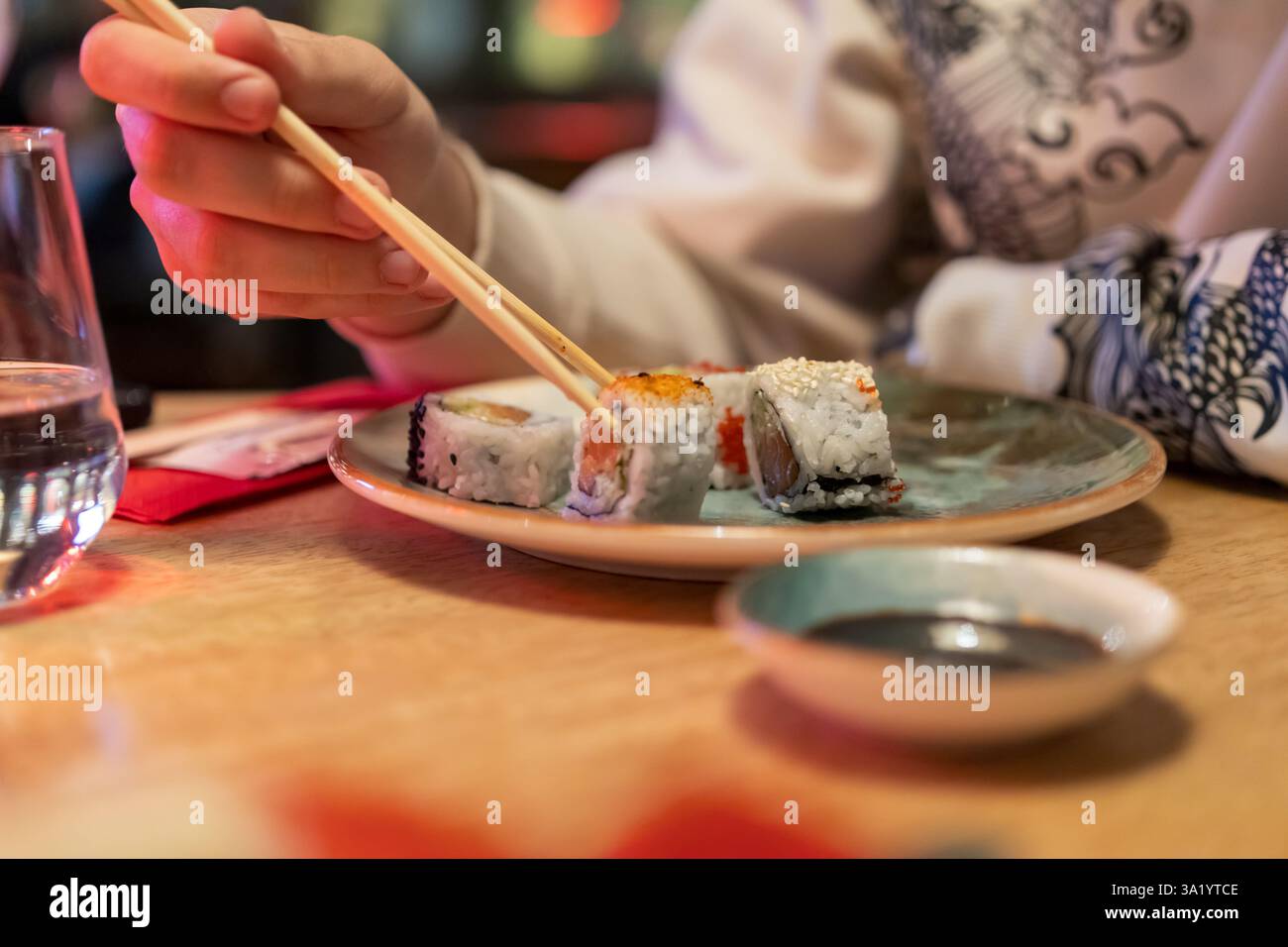 una persona che gusta un piatto di sushi, mettendo in risalto l'esperienza culinaria intima e informale. L'attenzione è concentrata sulla mano con le bacchette per raccogliere una torta Foto Stock