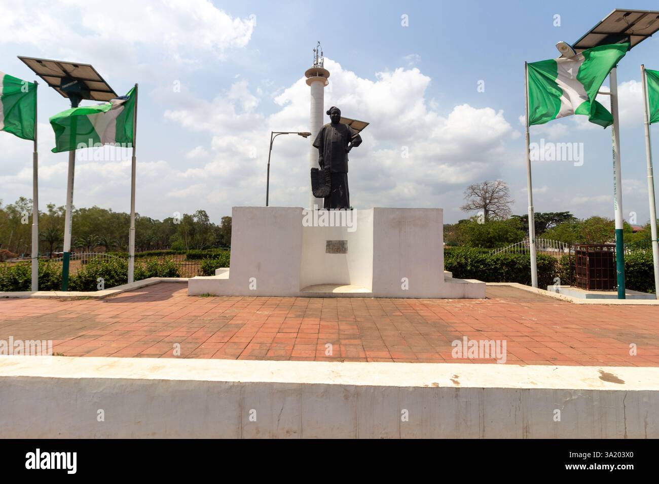Monumento a Enugu, Nigeria, con una figura di Michael Okpara su un piedistallo con bandiere e una torre sullo sfondo. Marzo 2025 Foto Stock