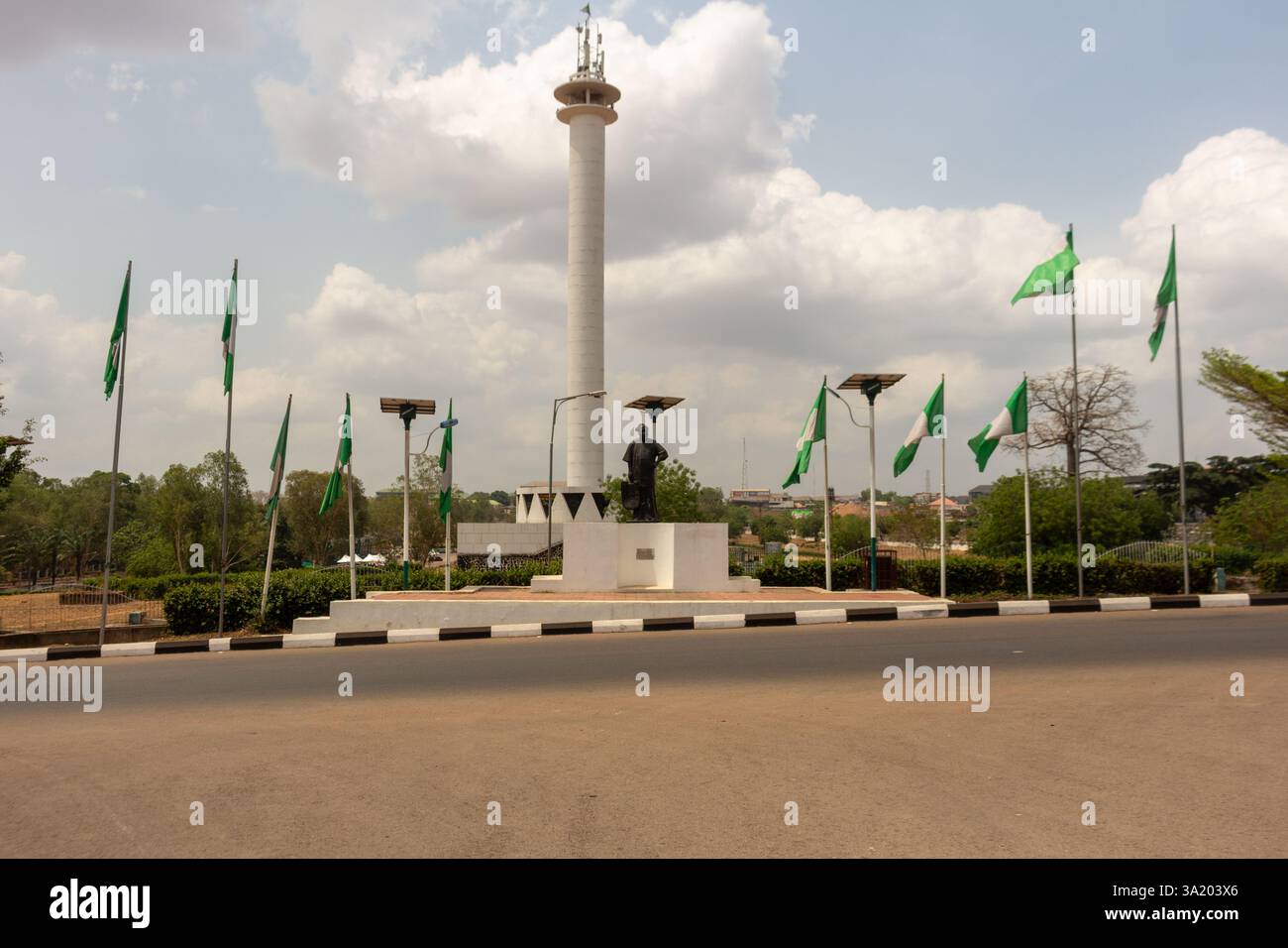 Monumento a Enugu, Nigeria, con una figura di Michael Okpara su un piedistallo con bandiere e una torre sullo sfondo. Marzo 2025 Foto Stock