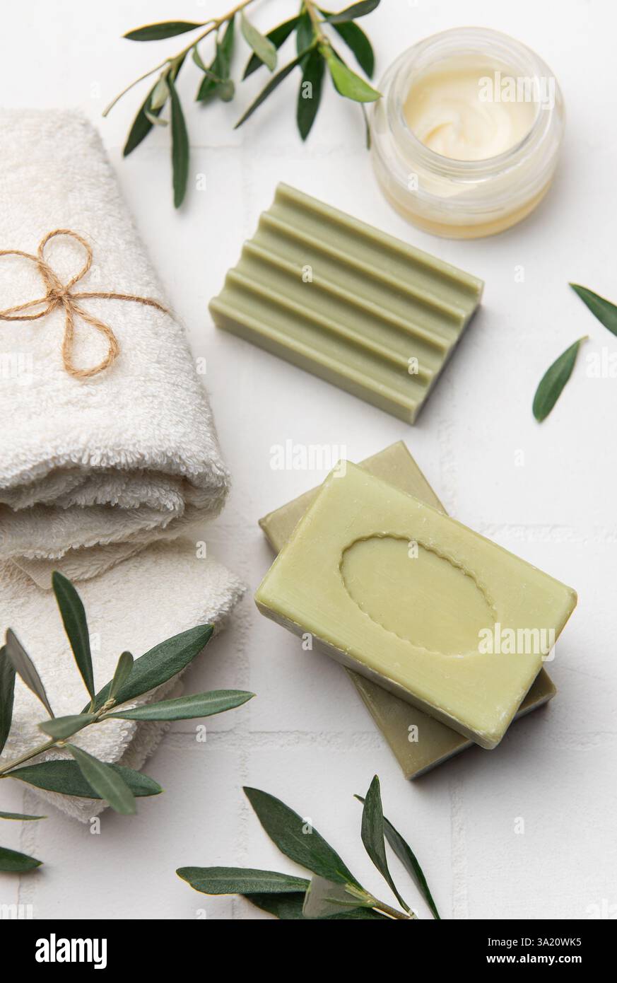 Saponette di olive naturali, crema idratante, ciuffi di ulivo freschi e morbidi asciugamani bianchi creano un rilassante ambiente spa Foto Stock