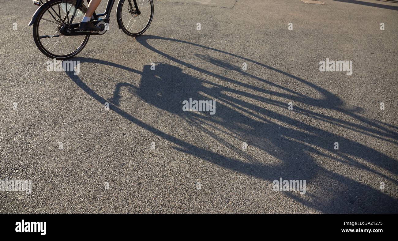 Nelle ore serali a Bucarest, un ciclista attraversa una zona vivace, mentre la luce calda proietta lunghe ombre sul marciapiede, catturando il vib Foto Stock