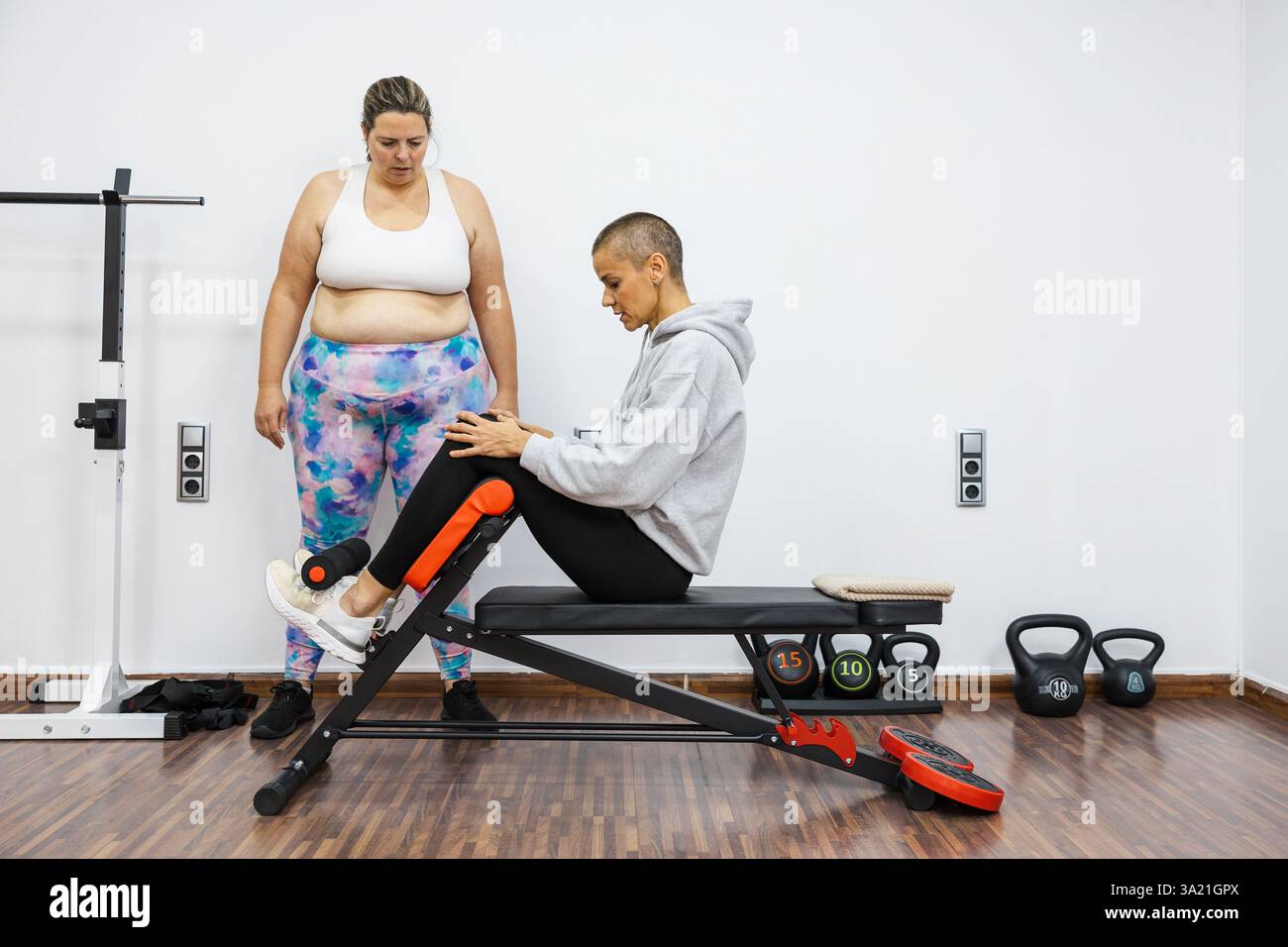 Personal trainer che guida il cliente attraverso esercizi addominali sulla panchina in palestra Foto Stock