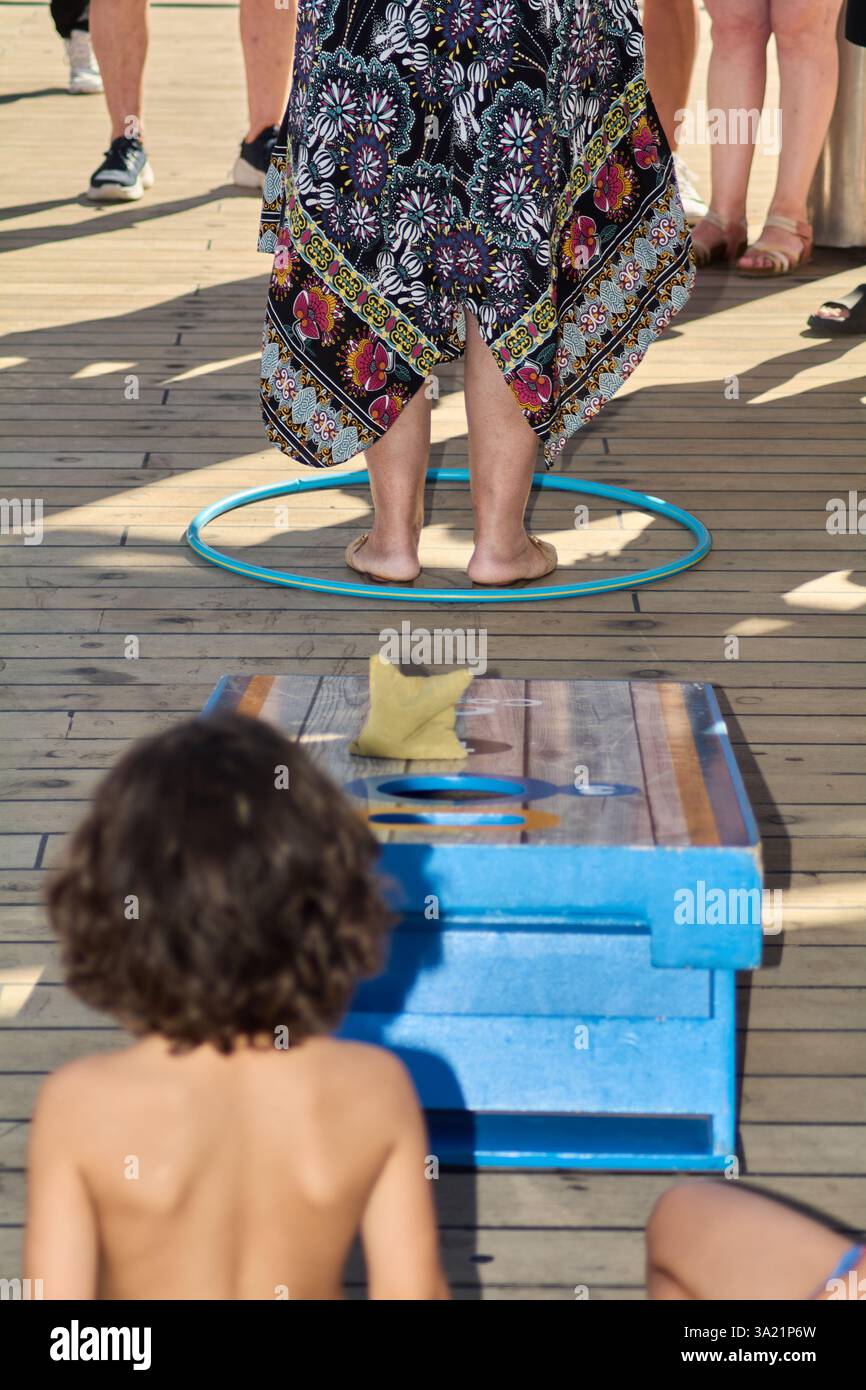 Catania. Italia - 11 marzo 2025: Gruppo affiatato di giovani giocatori e osservatori impegnati in una partita di cornhole spensierata, godendo l'outdoor condiviso Foto Stock