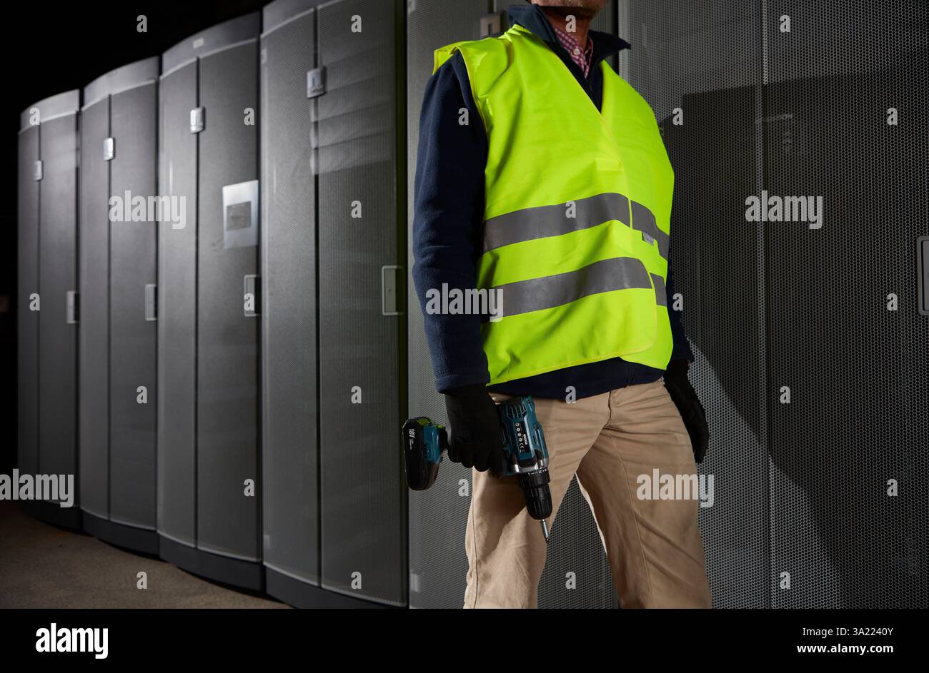 Addetto alla manutenzione con trapano a batteria, in piedi nella sala server. Foto Stock