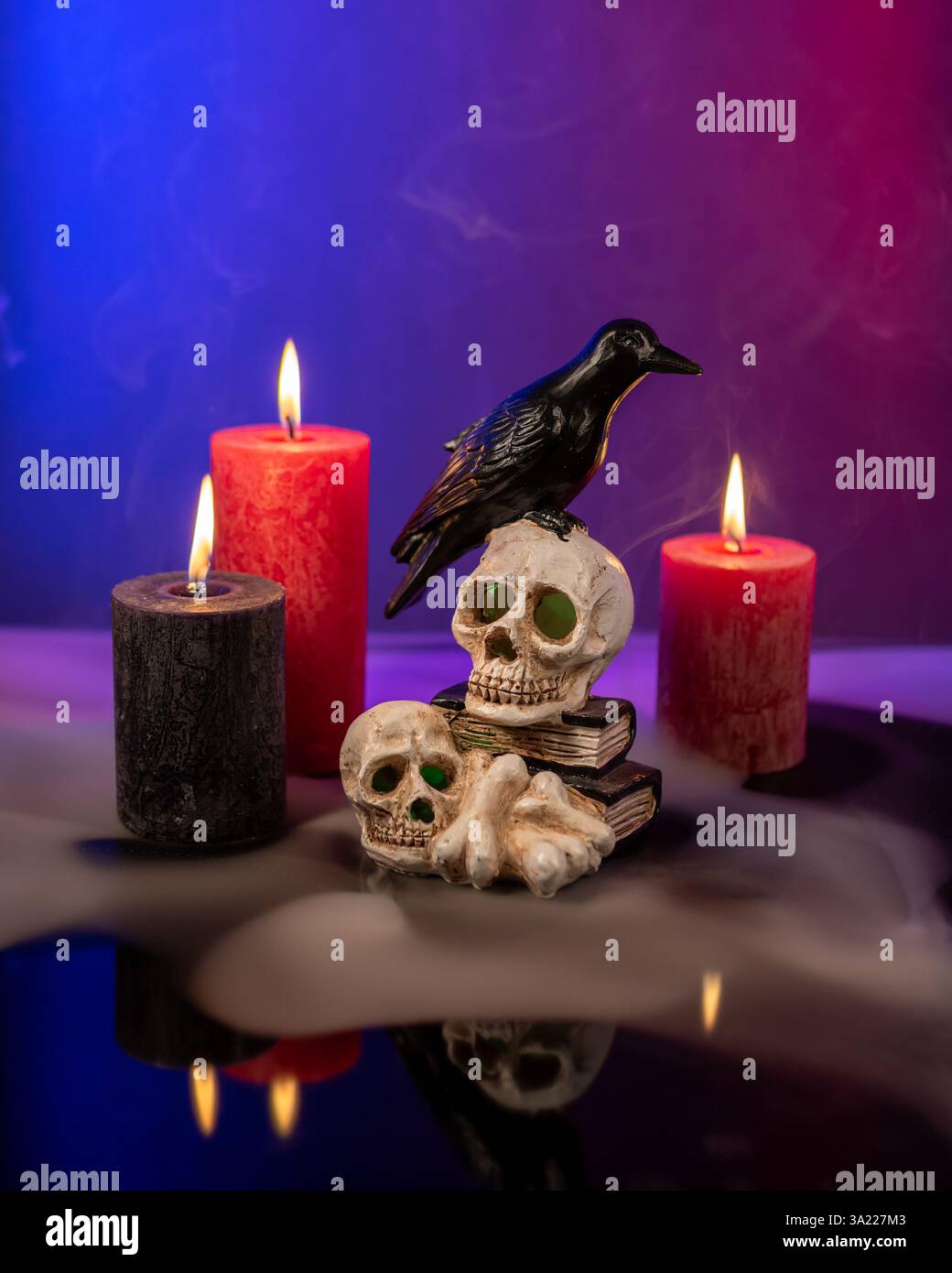 Figura di corvo seduta sui teschi e sulle ossa. Candele accese, luce mistica e fumo. Foto Stock