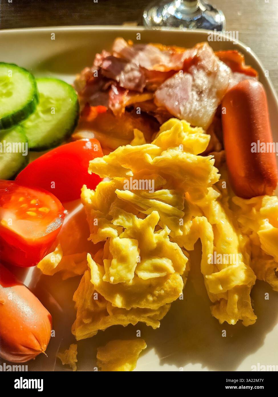 Uova strapazzate, pancetta croccante, salsicce e verdure fresche su piatto bianco. Foto di alta qualità Foto Stock