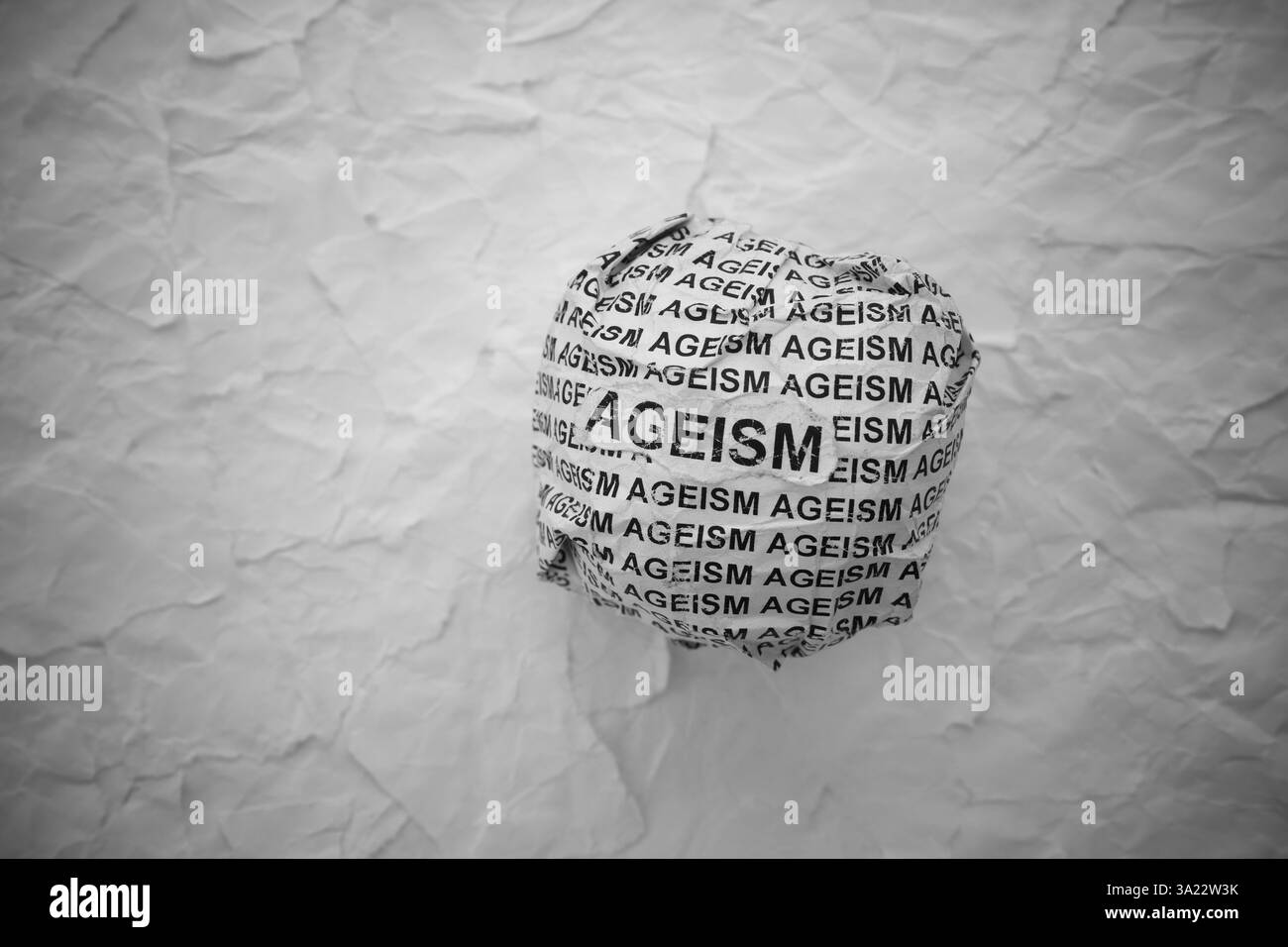 Palla di carta sgualcita con parole "ageism" su sfondo strappato di pezzi di carta bianca. Foto Stock