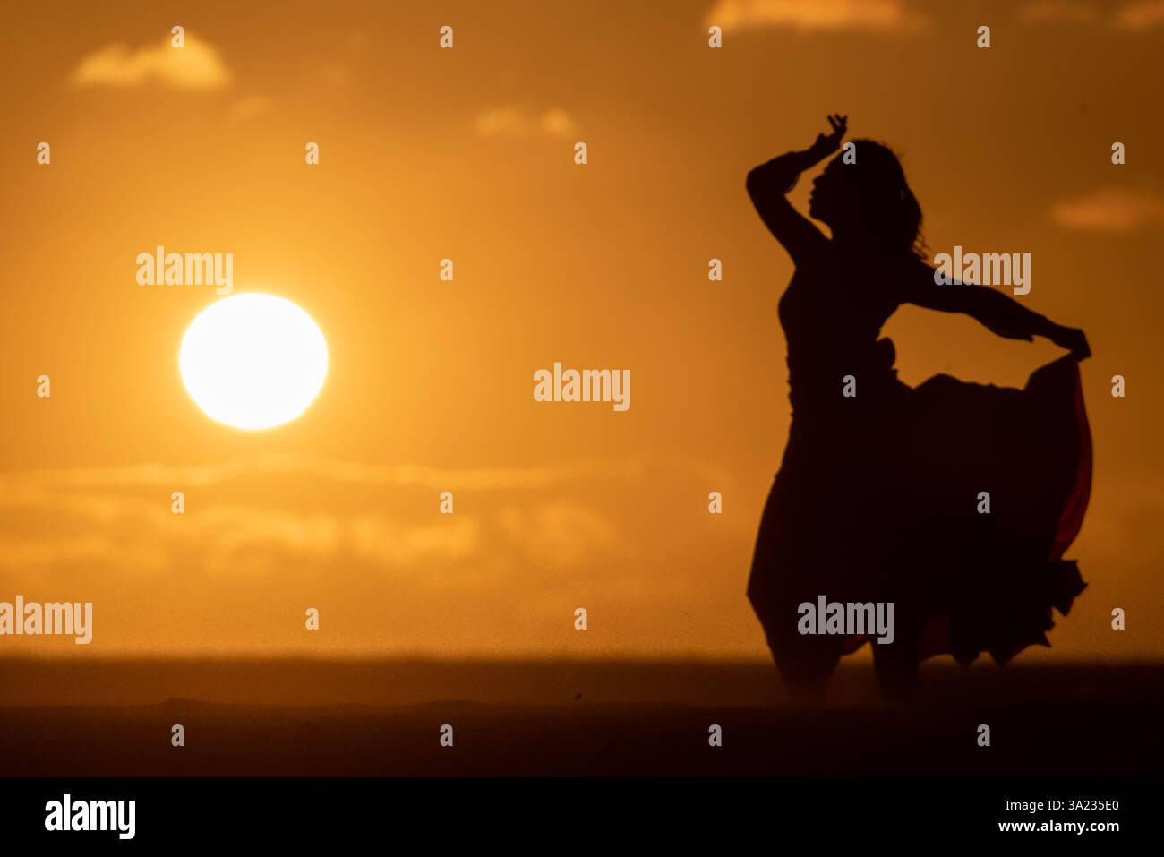 silhouette di una donna in abito fluente con le mani sulla testa al tramonto Foto Stock
