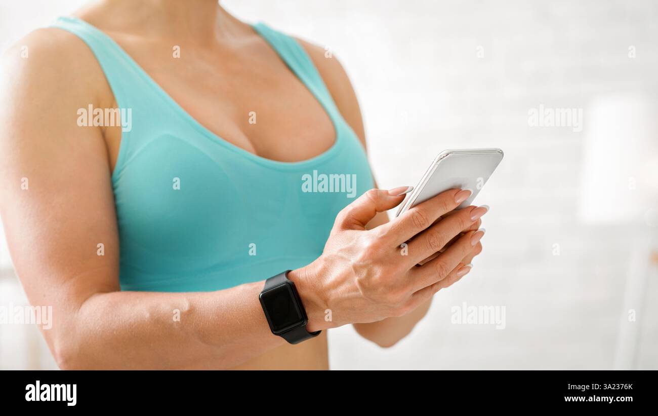 Palestra. Donna con orologio intelligente e telefono in mano in interni leggeri Foto Stock