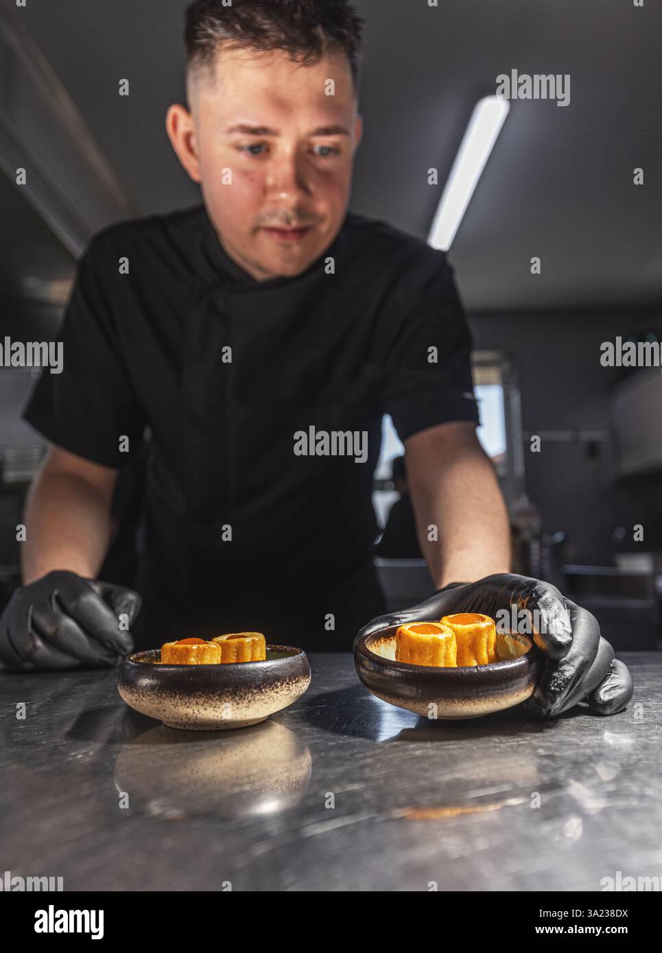 Chef professionista che serve antipasti eleganti in una cucina commerciale, enfatizzando la precisione culinaria e la presentazione del cibo Foto Stock