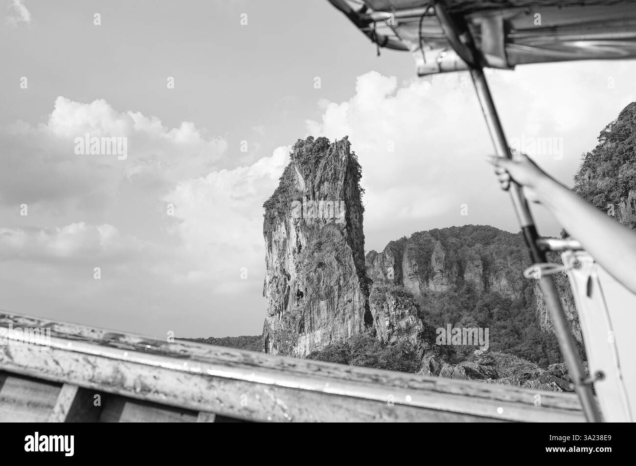 Una scogliera calcarea sorge dalla giungla, incorniciata dal bordo di una tradizionale barca a coda lunga in bianco e nero Foto Stock