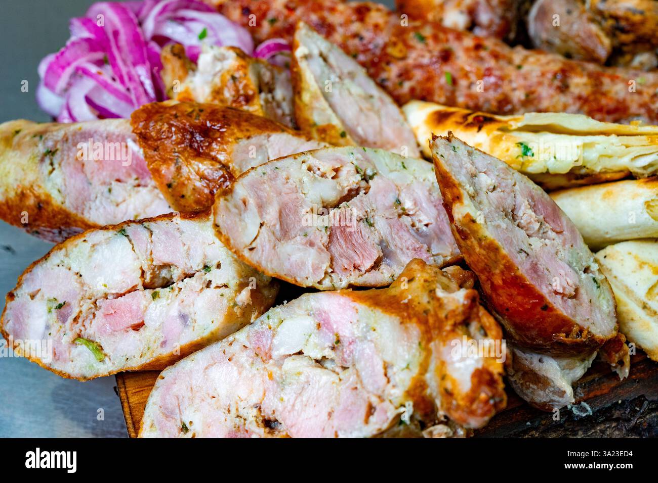 Un vivace assortimento di salsicce grigliate è placcato, mostrando un mix di consistenze e sapori. Le cipolle fresche aggiungono colore, mentre il pane caldo accompagna il Foto Stock