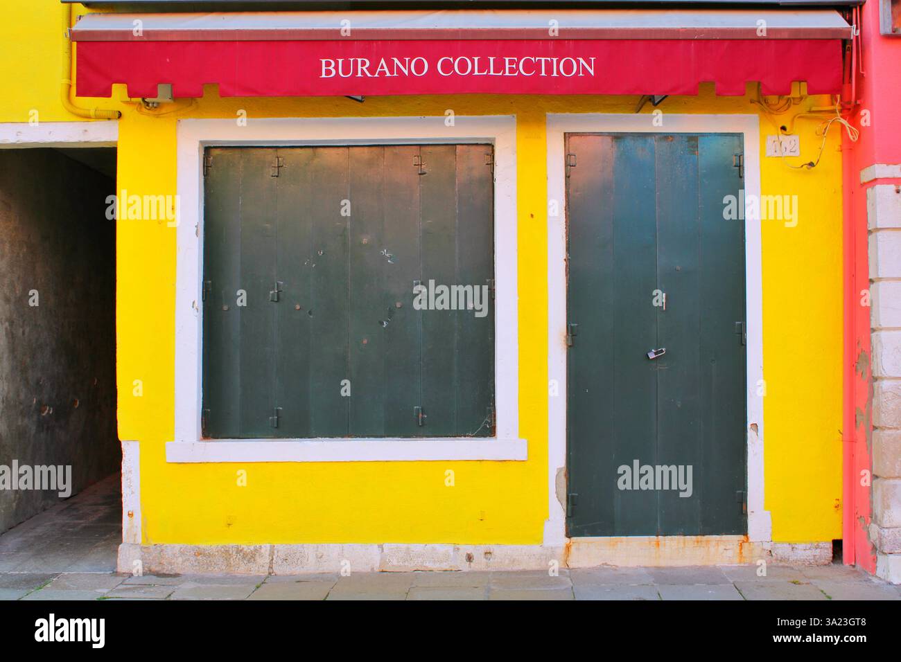 Burano, Italia - 26/01/2023. Un punto vendita chiuso con una tenda rossa che recita "Burano Collection" su una facciata gialla, che mostra lo stile colorato dell'isola. Foto Stock