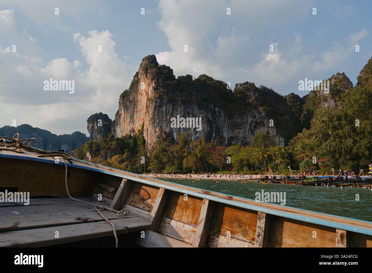 Una tradizionale barca in legno scivola verso Railay Beach, dove le scogliere calcaree si innalzano su sabbie dorate e acque turchesi Foto Stock