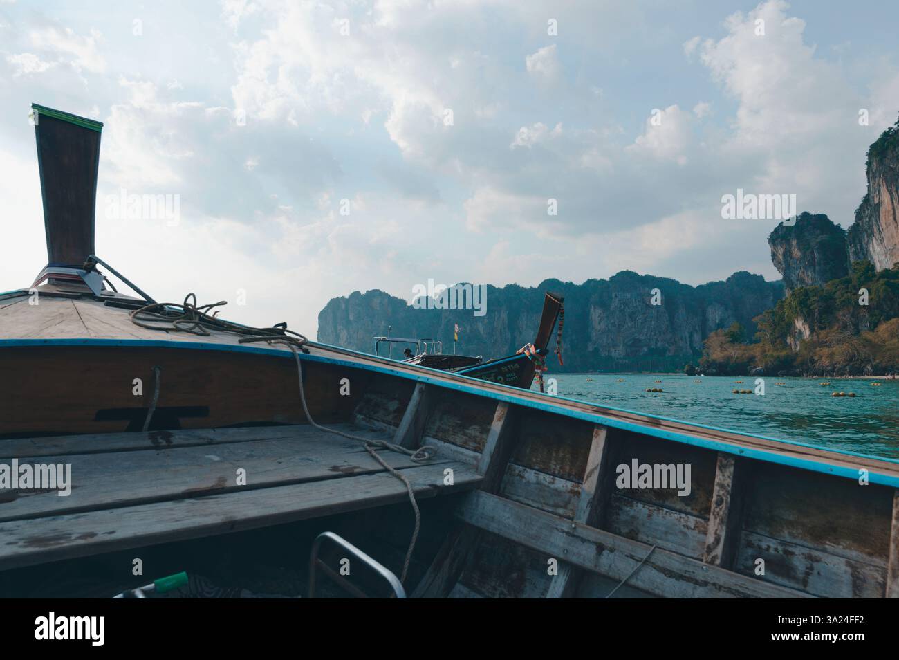 Le tradizionali barche in legno galleggiano sulle acque turchesi vicino alle torreggianti scogliere calcaree di Railay Foto Stock