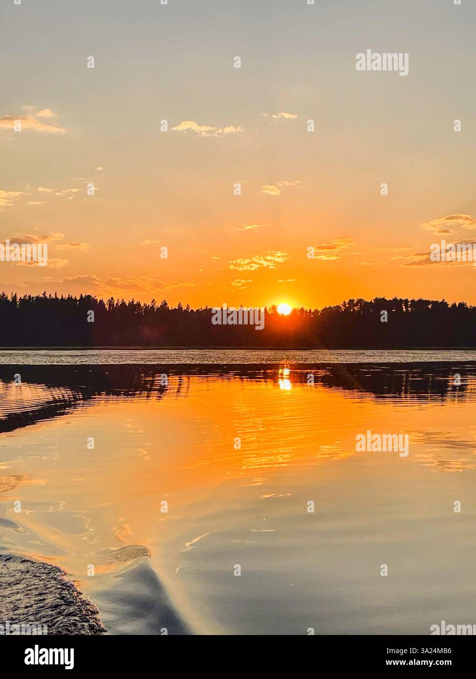 Il sole tramonta su un lago calmo, proiettando un intenso bagliore arancione sul cielo e sull'acqua. Il riflesso crea un effetto speculare sorprendente, evidenziando - Immagine stock catturata con smartphone