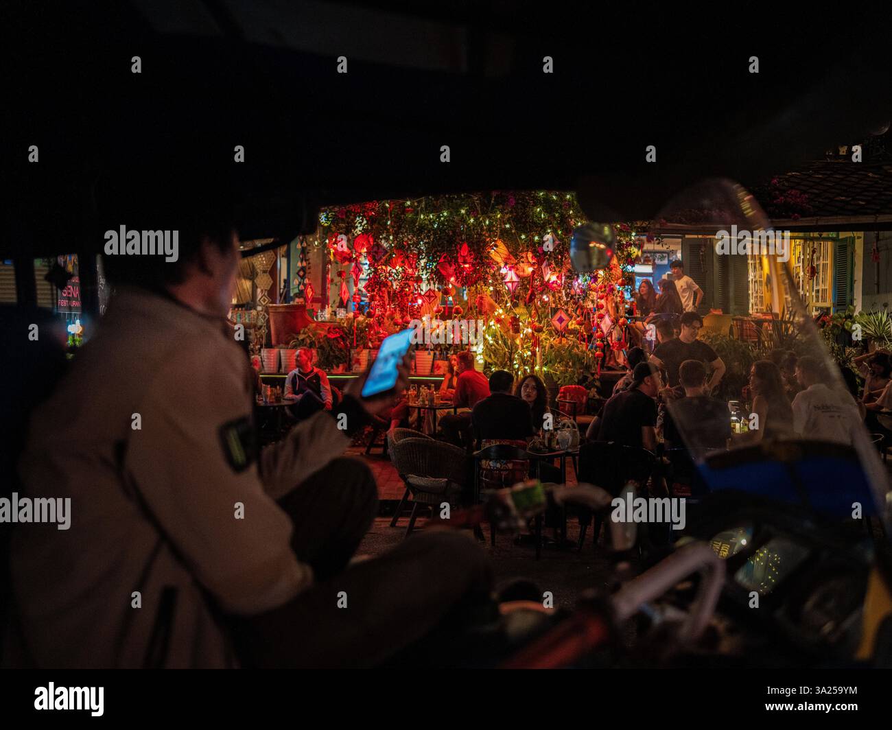 Autista di tuk-tuk a Luang Prabang, Laos, in attesa dei passeggeri sotto le luci soffuse della notte Foto Stock
