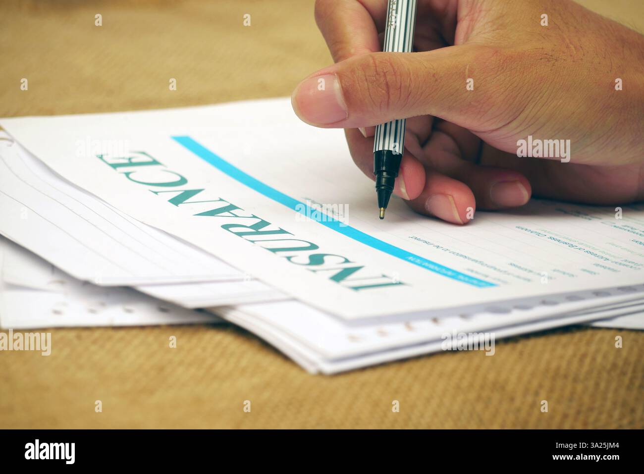 Tenere a mano la penna compilando il modulo di assicurazione sulla superficie della documentazione. Foto Stock