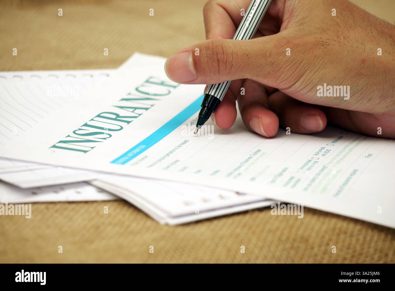 Tenere a mano la penna compilando il modulo di assicurazione sulla superficie della documentazione. Foto Stock