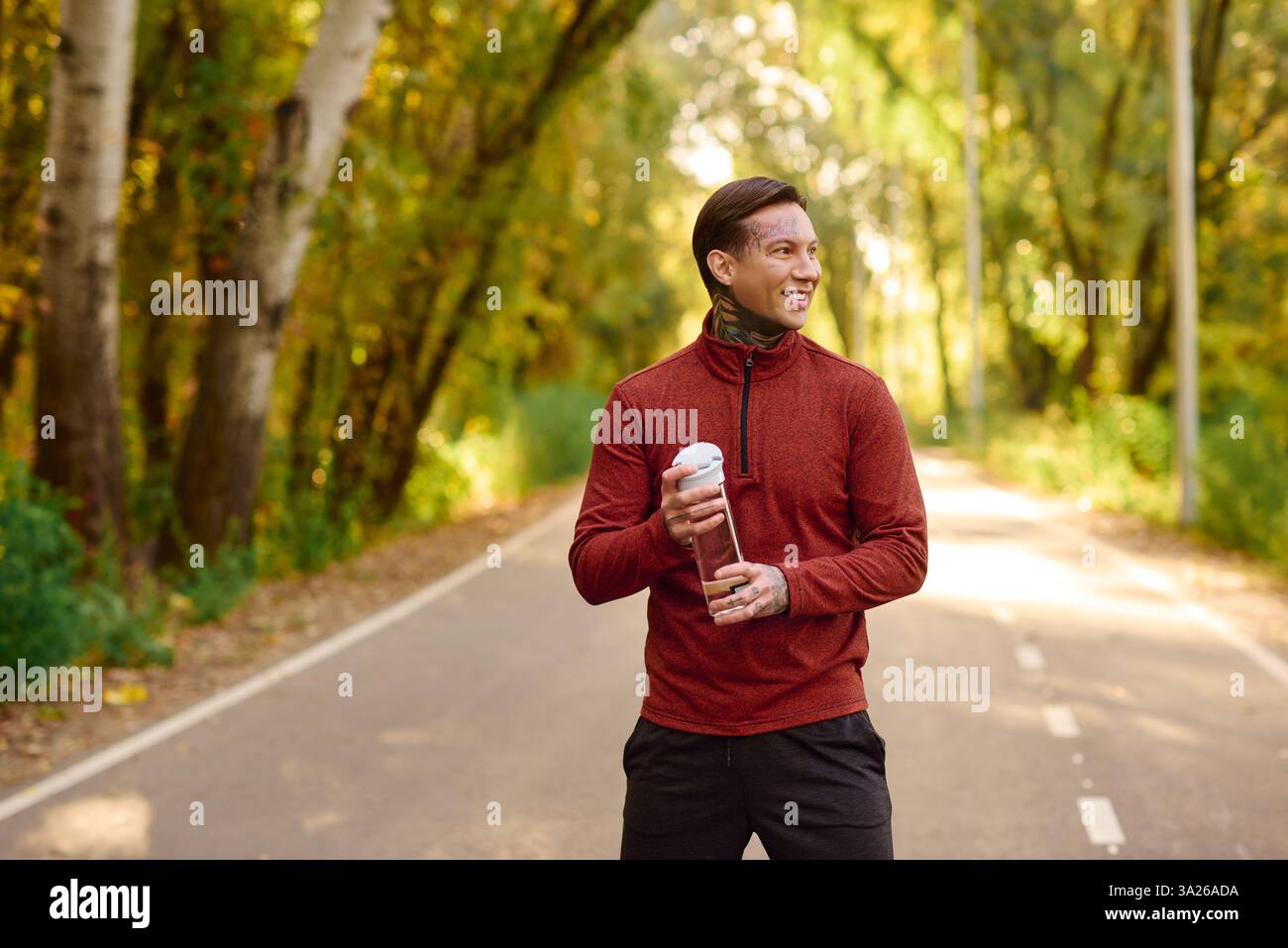 Un elegante trendsetter sorride in una foresta vibrante, bevi in mano. Foto Stock