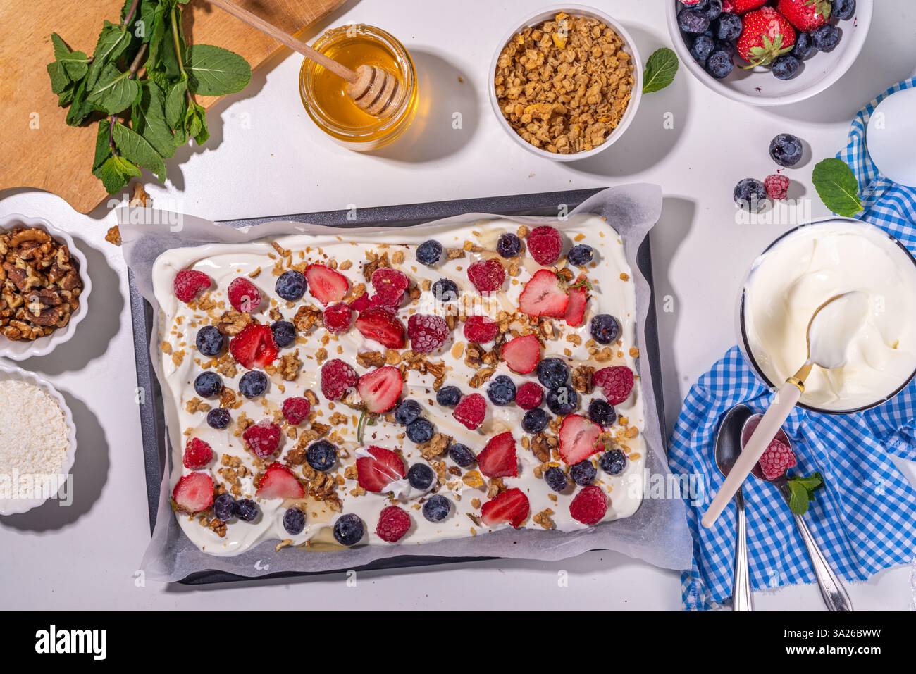 Preparazione della cottura con sfondo di corteccia di yogurt congelato con yogurt greco, bacche fresche, muesli, miele, salsa al cioccolato, con vassoio da forno deco. Vista dall'alto della donna Foto Stock