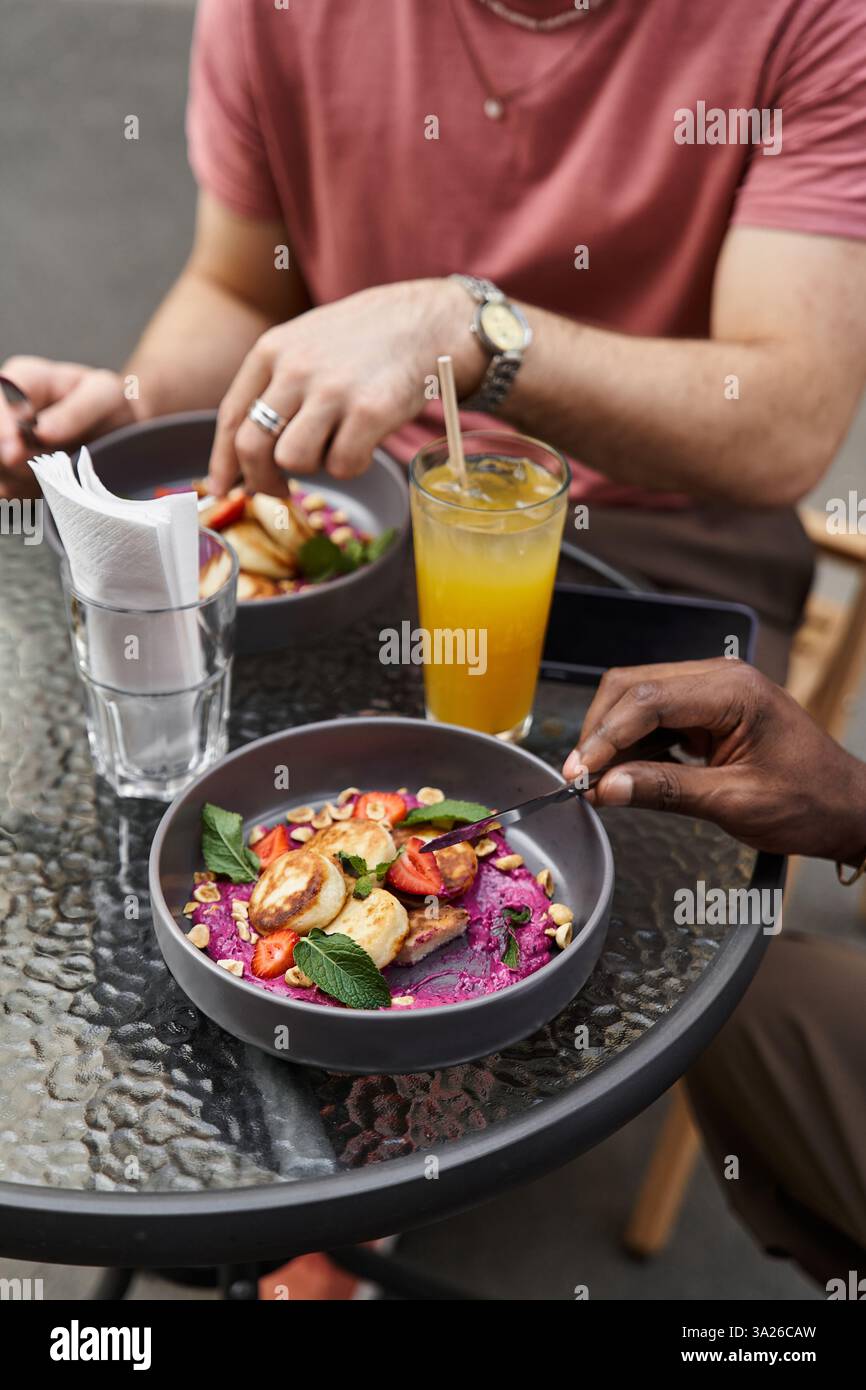 Due bellissimi individui condividono un momento di gioia con un pasto vibrante e una bevanda rinfrescante in un caffè. Foto Stock