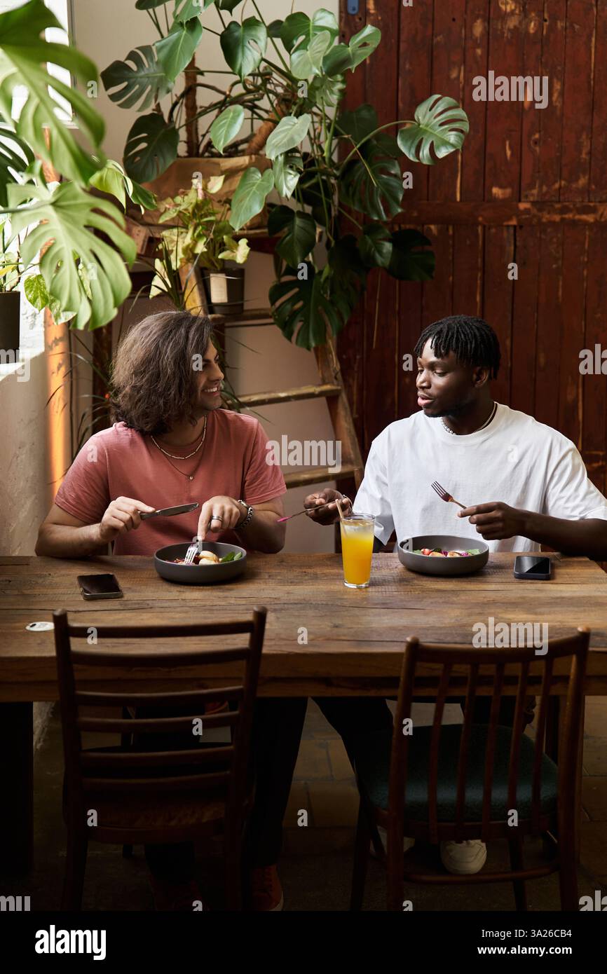 Due bellissimi individui condividono un pasto gioioso, ridendo e coinvolgendo in una conversazione sentita. Foto Stock