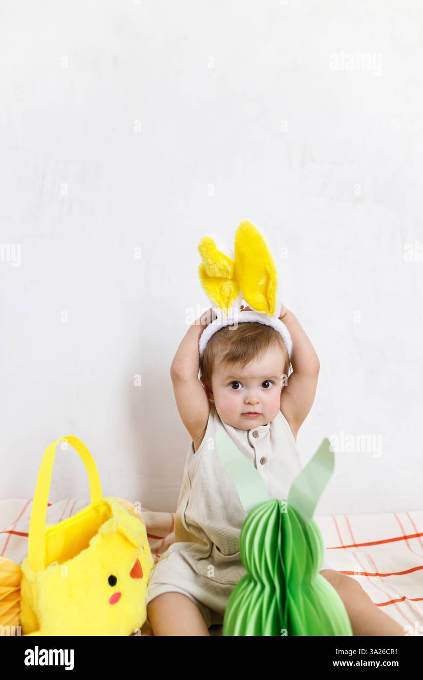 Buona Pasqua! Simpatico e simpatico bambino con orecchie da coniglio seduto con uova di carta pasquale colorate, decorazioni natalizie e carote. Adorabile coniglietto di Pasqua e Pasqua Foto Stock