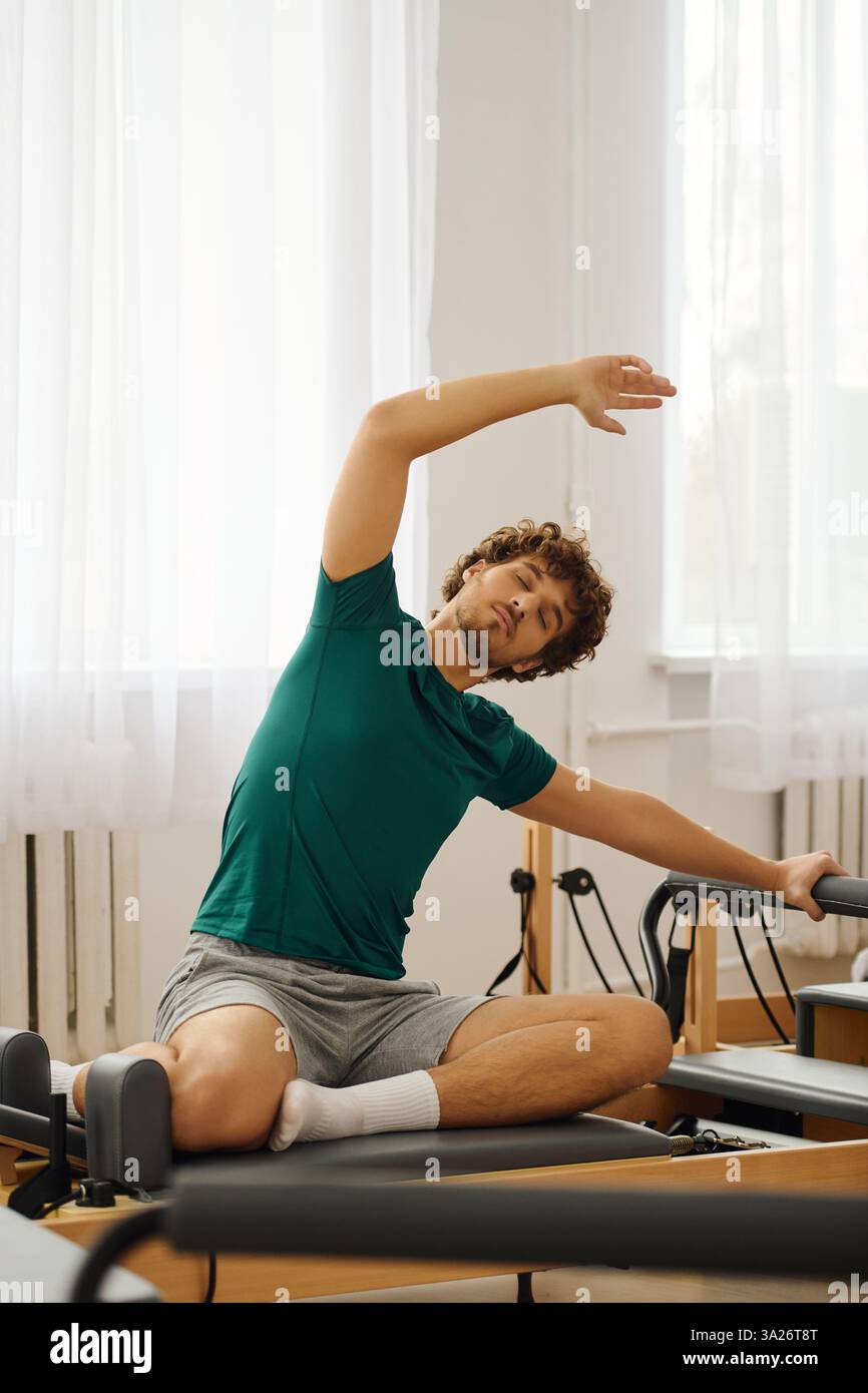 Una persona pratica stretching ed esercizi di base su un riformatore in uno studio luminoso. Foto Stock