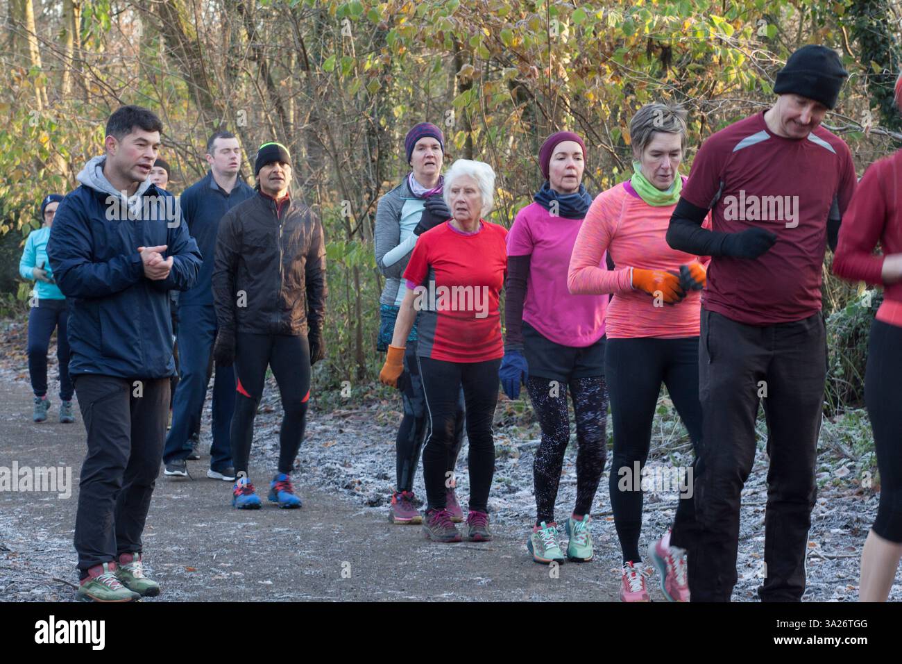 Un gruppo diversificato di adulti vestiti da atletica partecipa a un esercizio di gruppo all'aperto in un ambiente forestale. Sale Water Park, Manchester, Regno Unito Foto Stock
